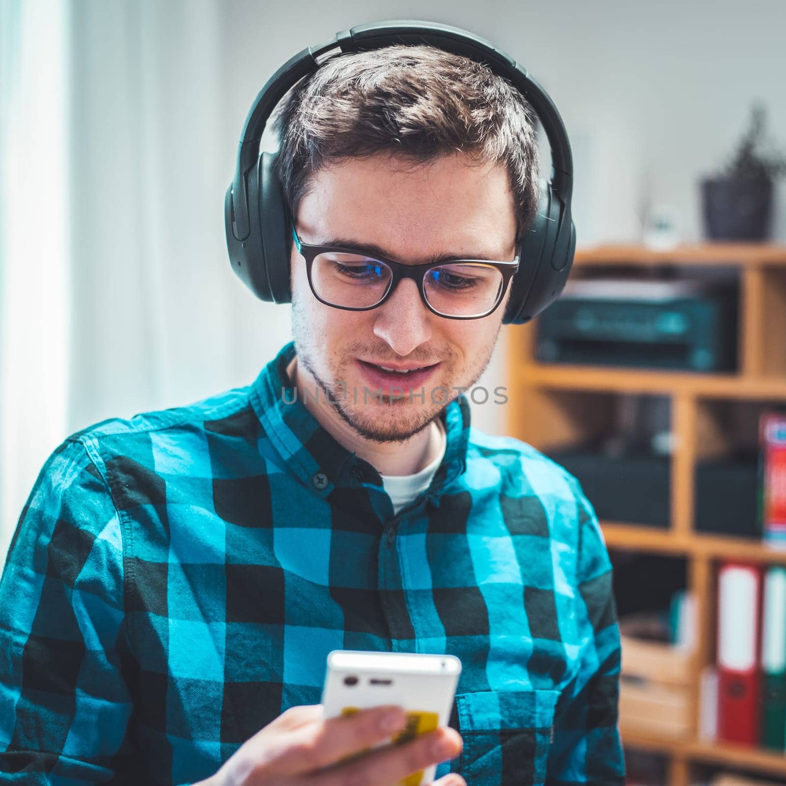 Young Caucasian man with checked blue shirt is listing to music with wireless headphones