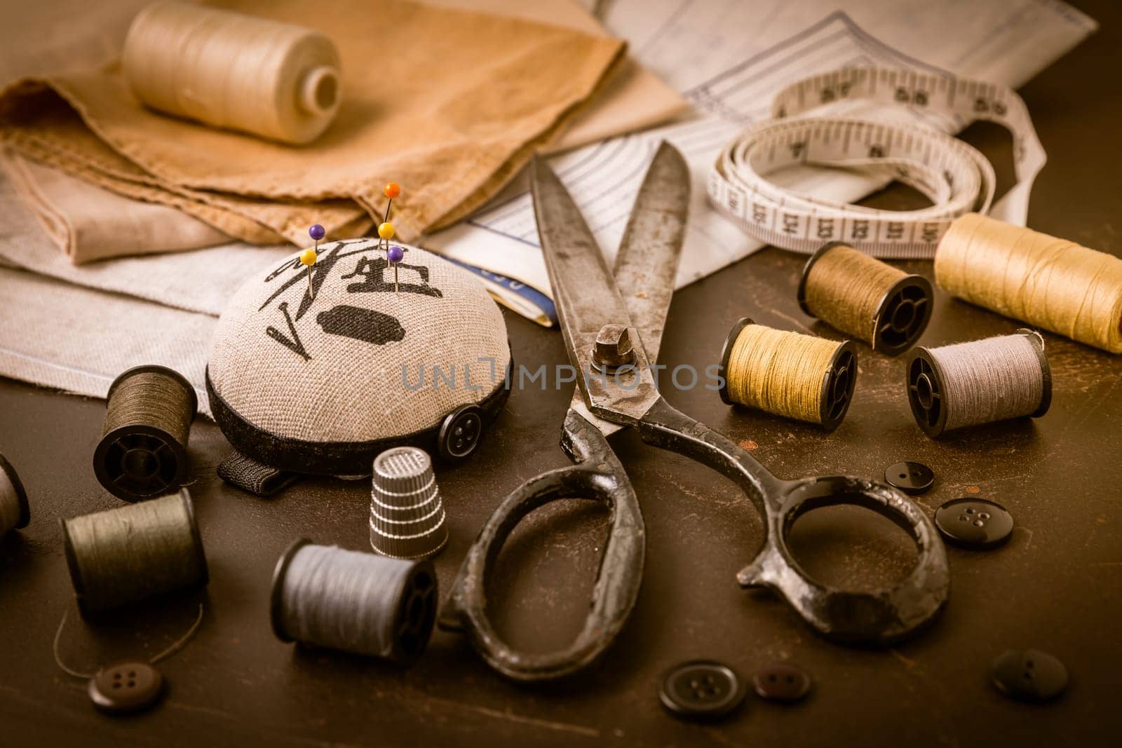 Sewing and craft tools - old scissors, bobbins with thread and needles on wooden table in vintage style