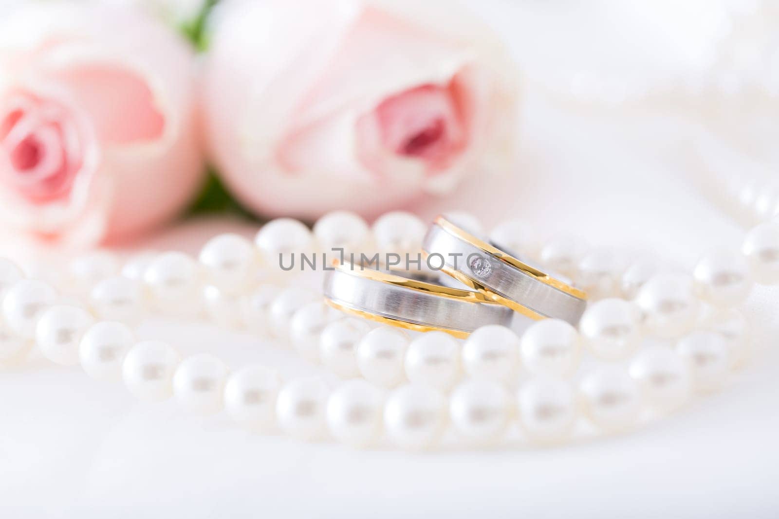 Modern wedding rings with pearl necklace wih pink roses in the background, soft focus