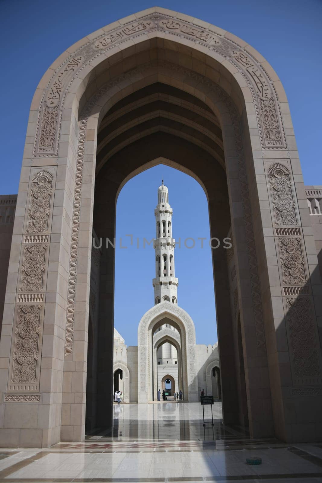 Archway with the Arabic inscription Great Sultan Qaboos Mosque and the main minaret in a visual axis. It is considered to be one of the most important buildings in the Sultanate of Oman.