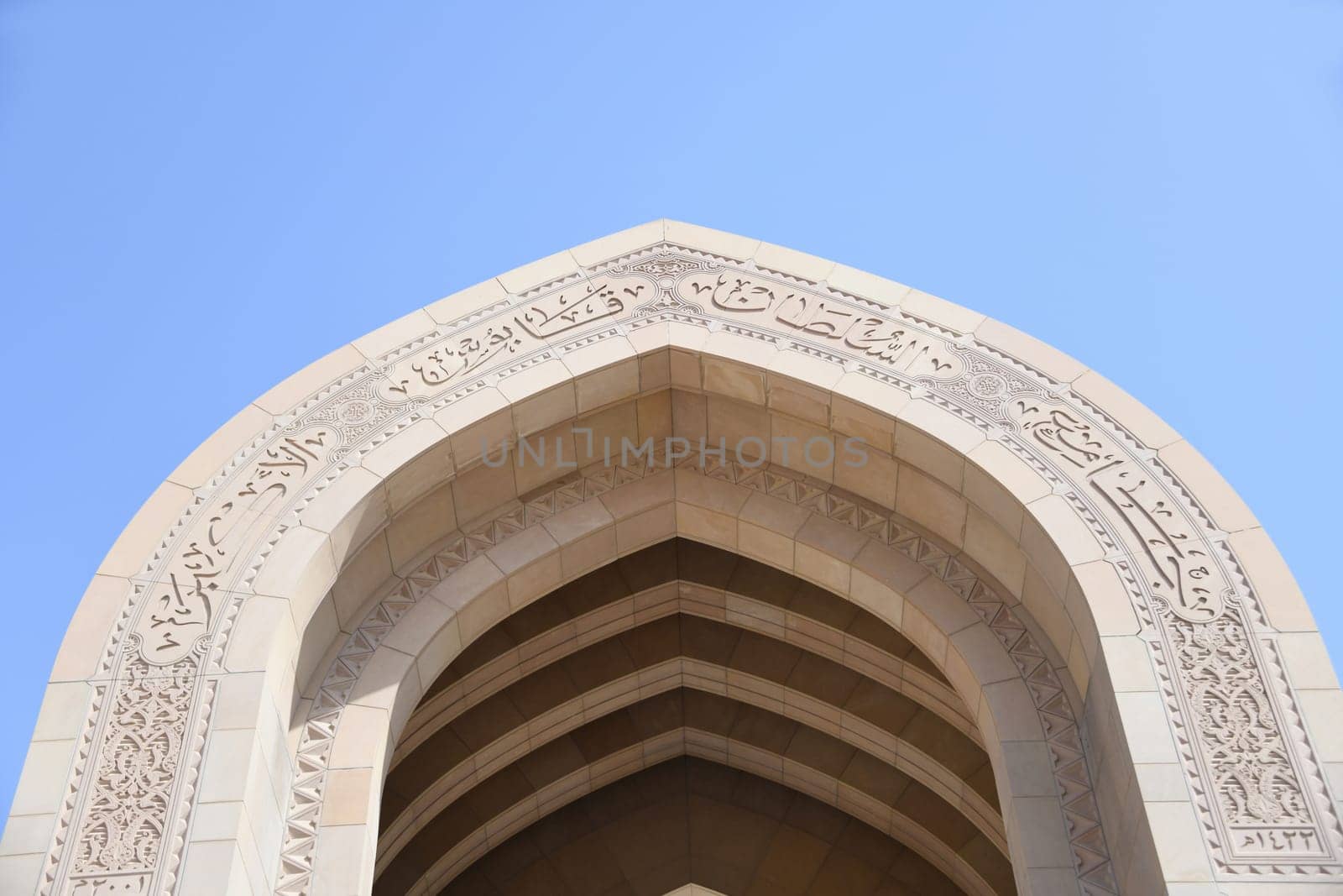 Archway with the Arabic inscription Great Sultan Qaboos Mosque and the main minaret in a visual axis. It is considered to be one of the most important buildings in the Sultanate of Oman.