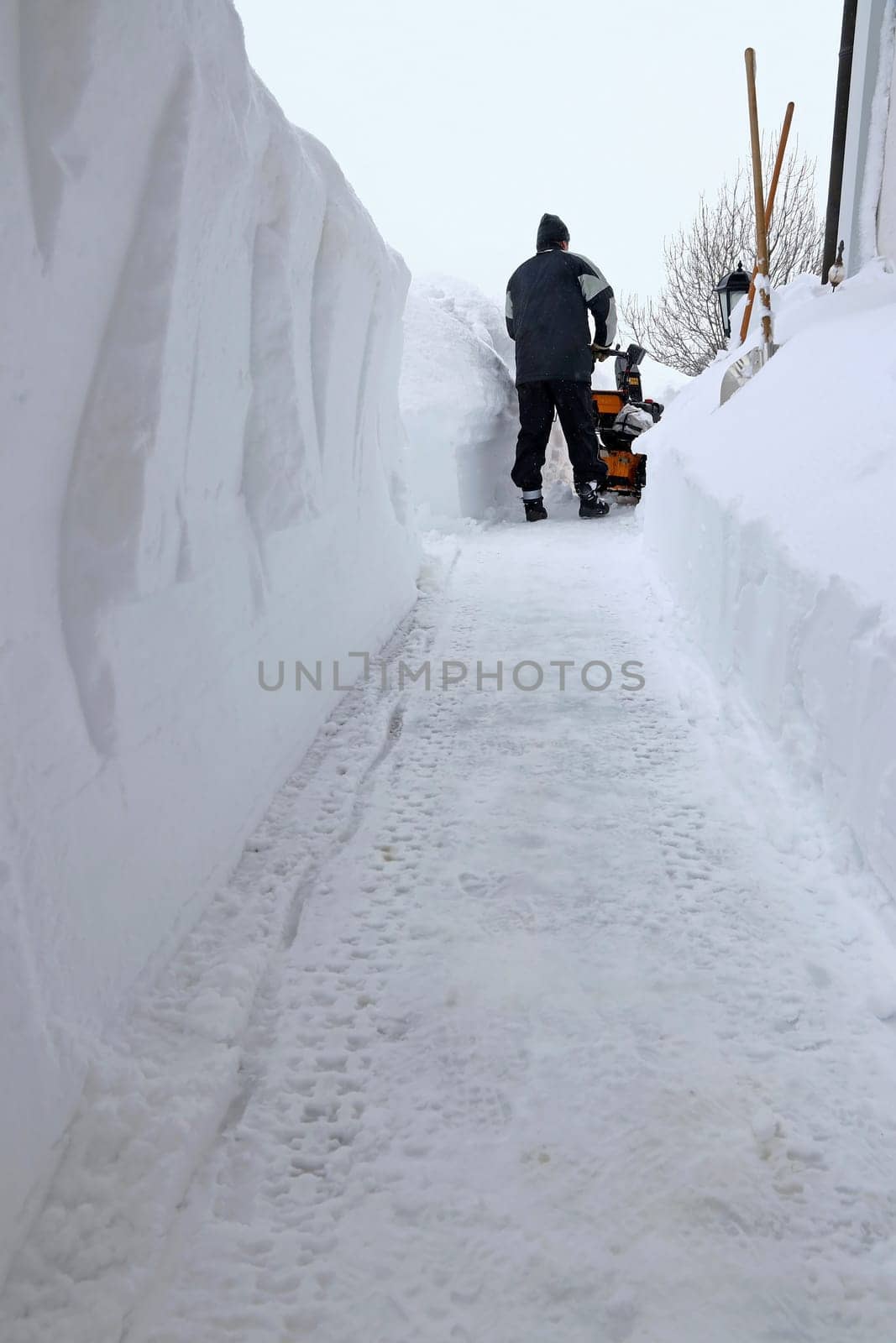 A man clears the sidewalk with a snow blower during heavy snowfall