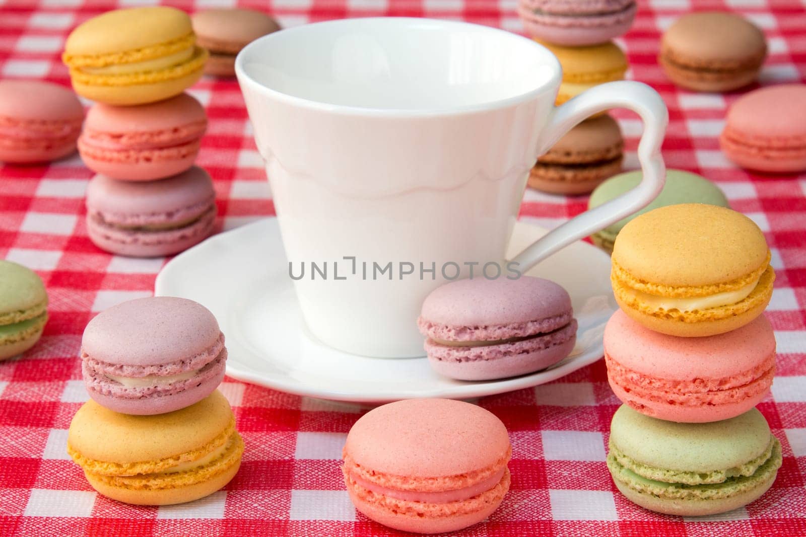Delicious french macaroons and white cup on the checkered tablecloth
