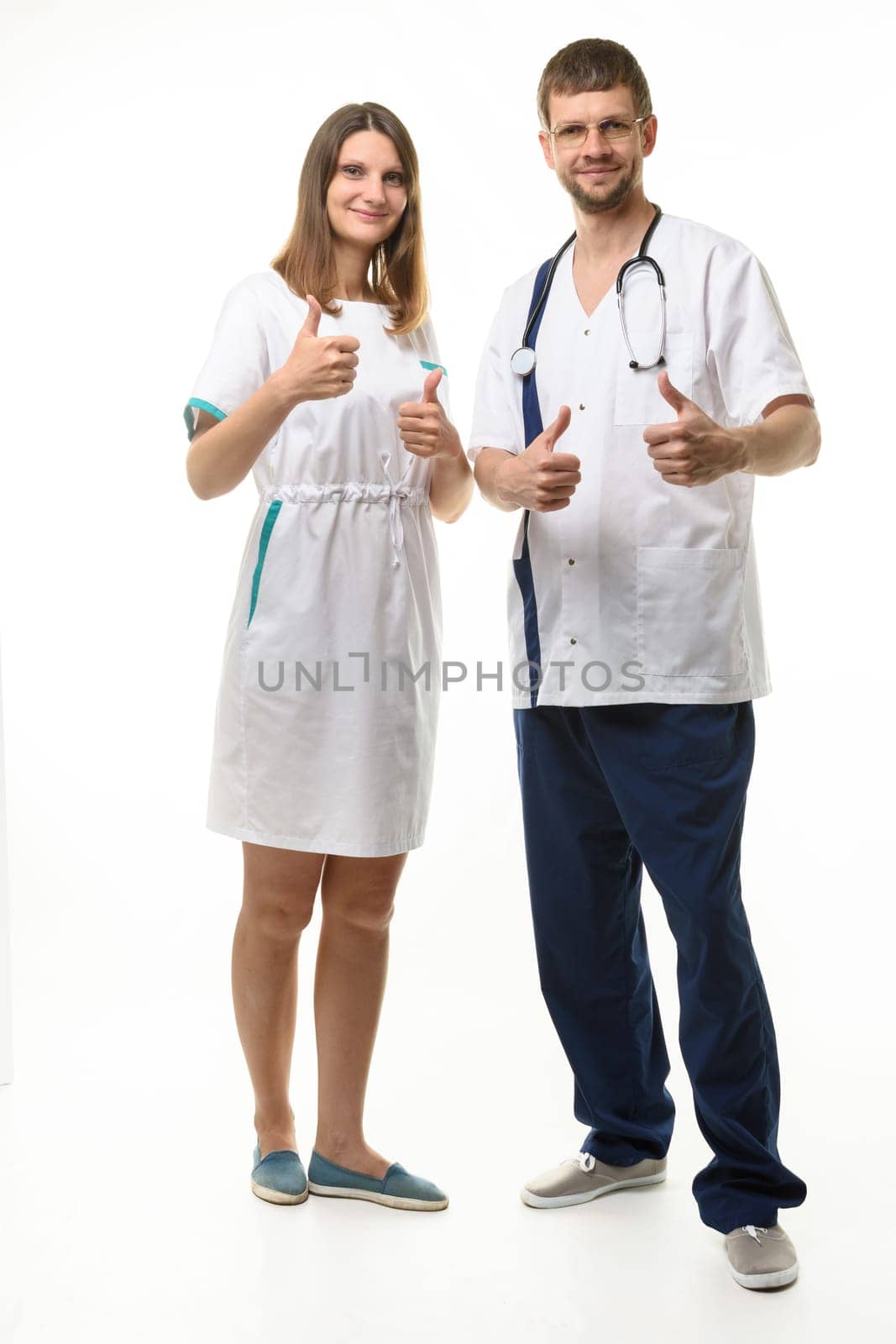 Doctor and nurse show thumbs up gesture with two hands and look happily into the frame