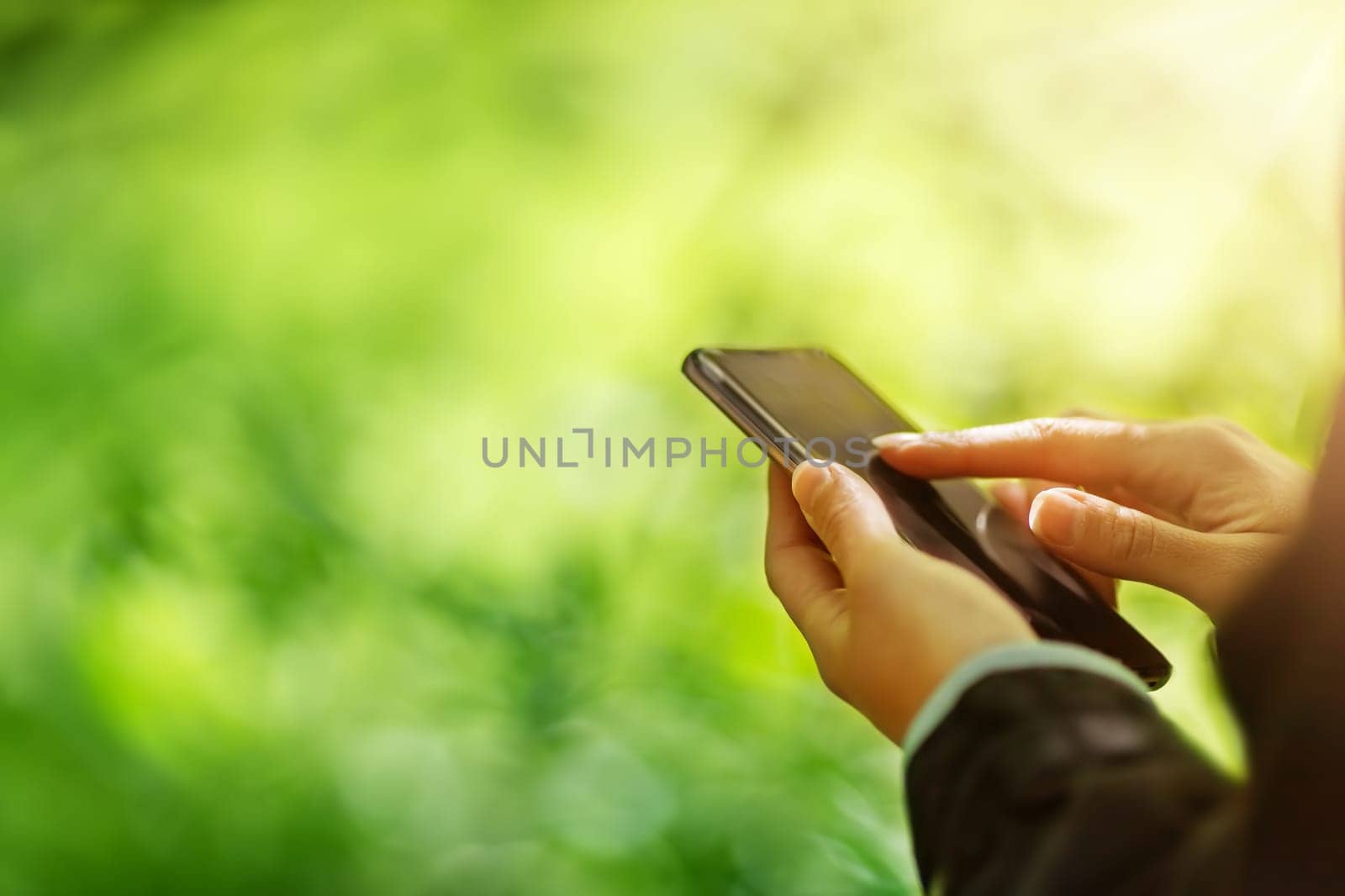Young woman on nature using her smartphone. Typing message on the phone. Internet online concept.