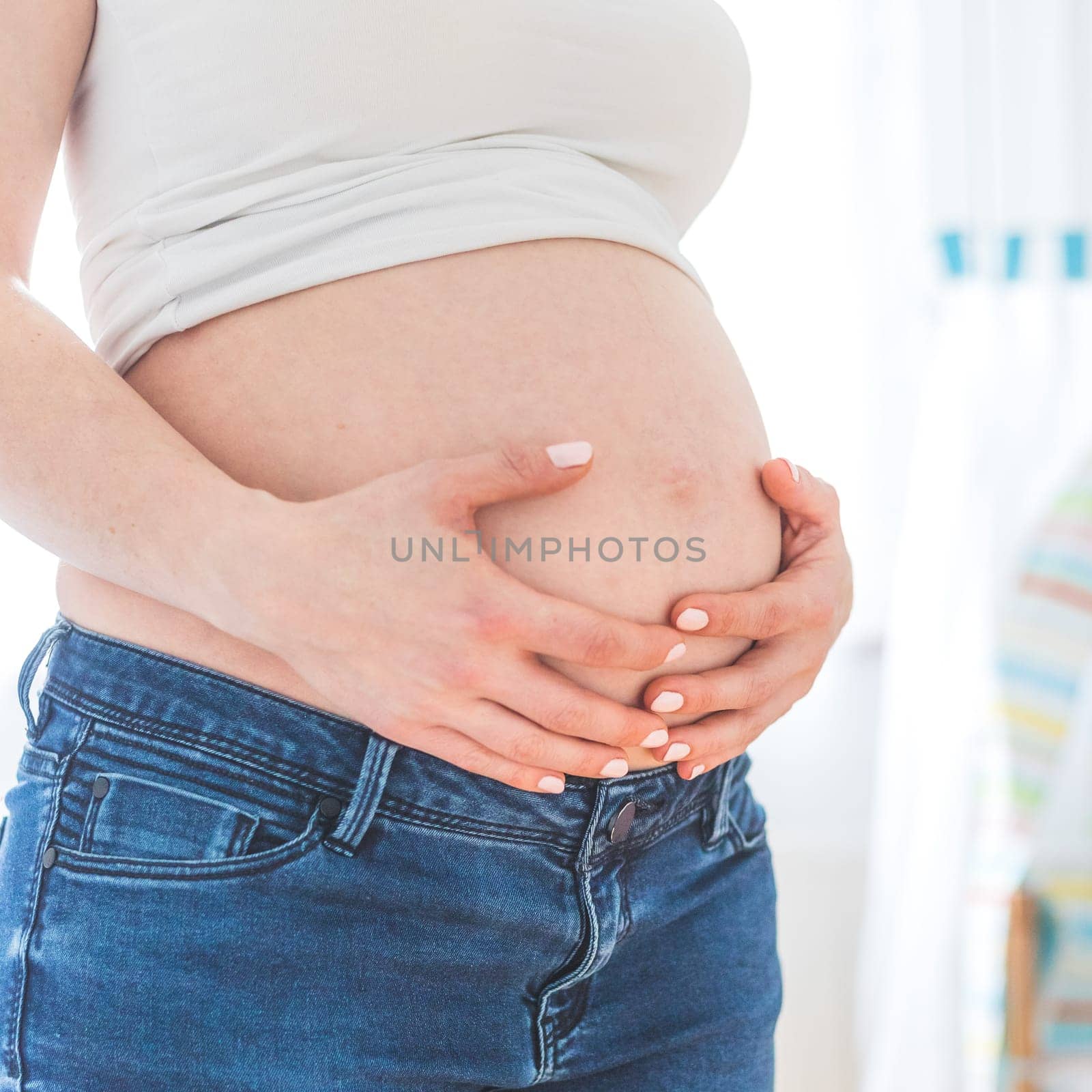 Caucasian pregnant mother touching her naked tummy, blue jeans, close up