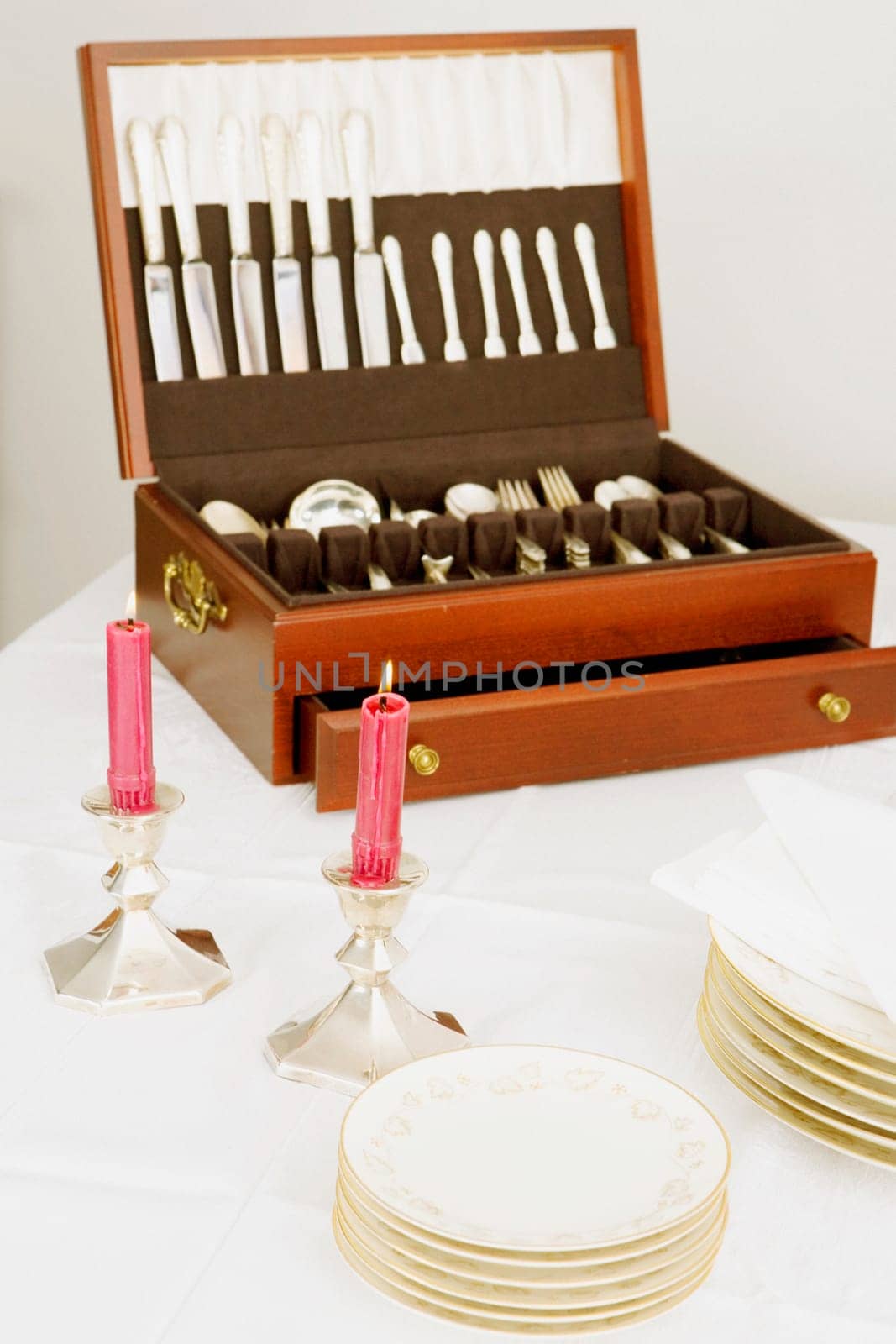 Two burning candles with a cutlery box and stacks of plates on a dining table