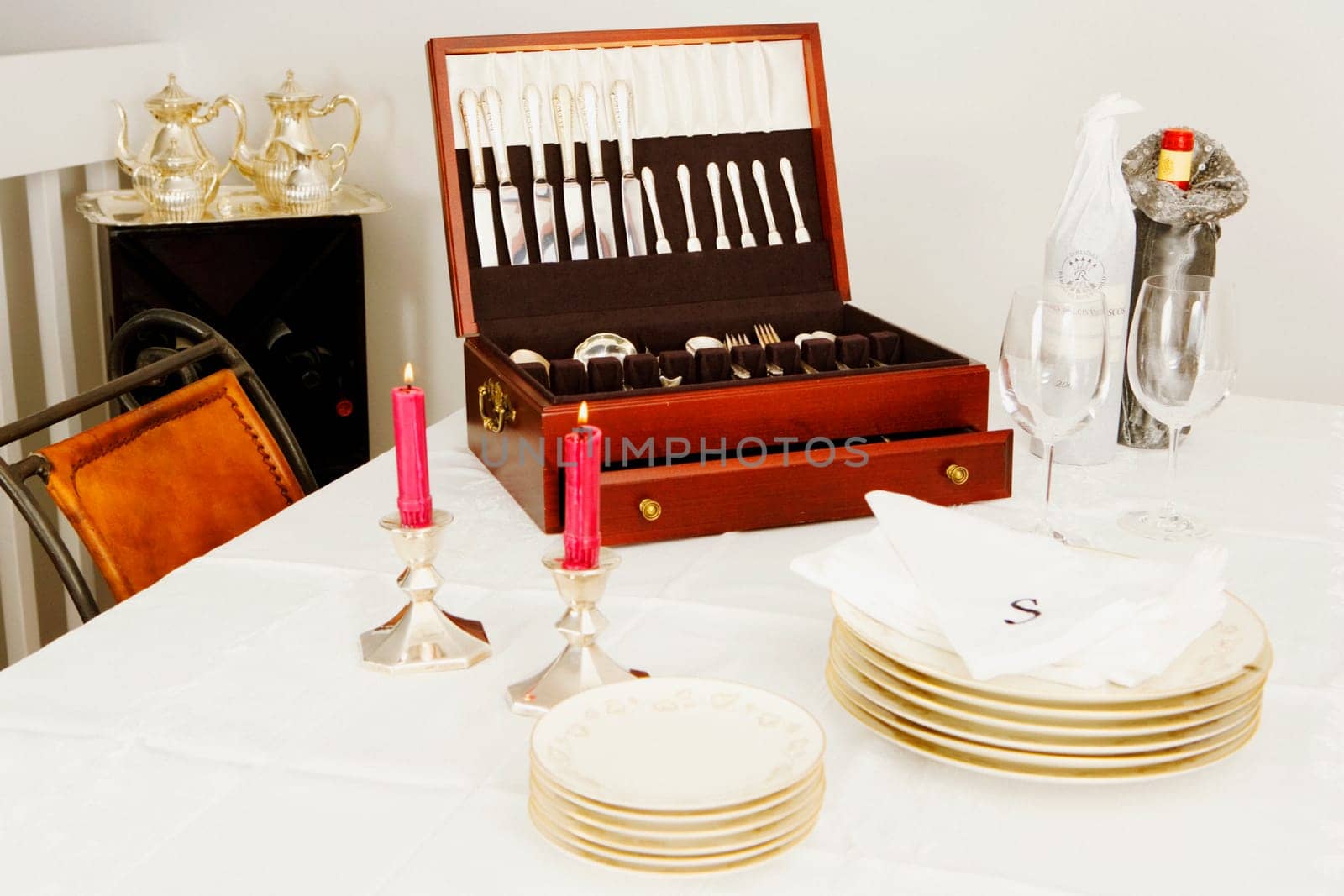 Two burning candles with a cutlery box and stacks of plates on a dining table