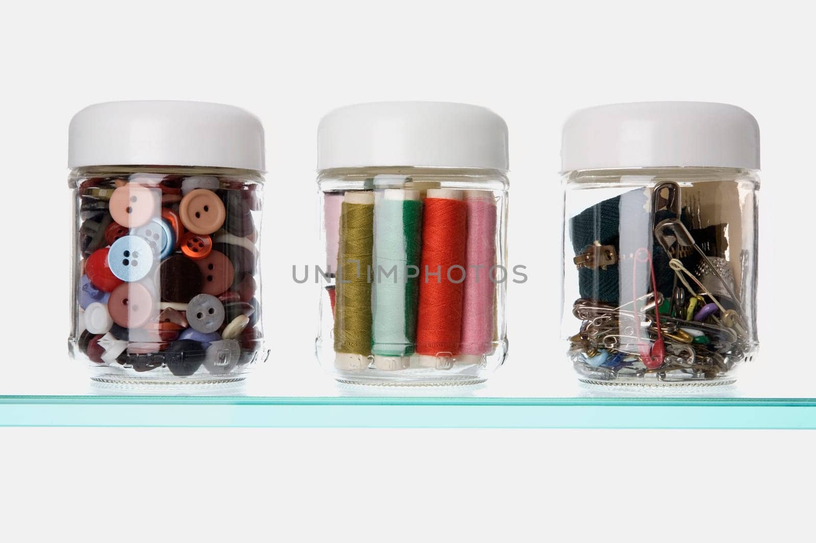 Close-up of buttons and safety pins with thread spools in three different jars