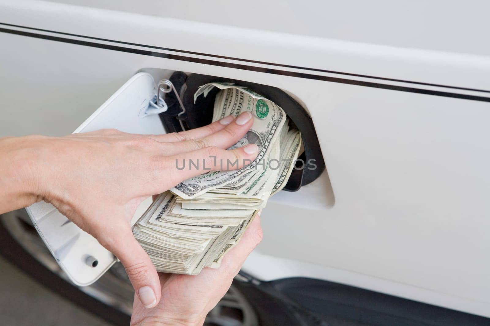 Close_up of a personŽs hands putting US paper currency in a gas tank of a car