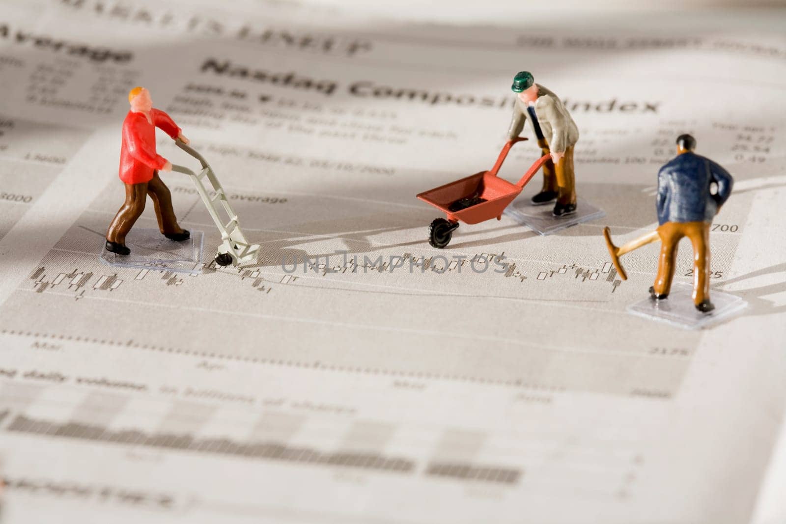 Figurines of manual workers working on a financial newspaper