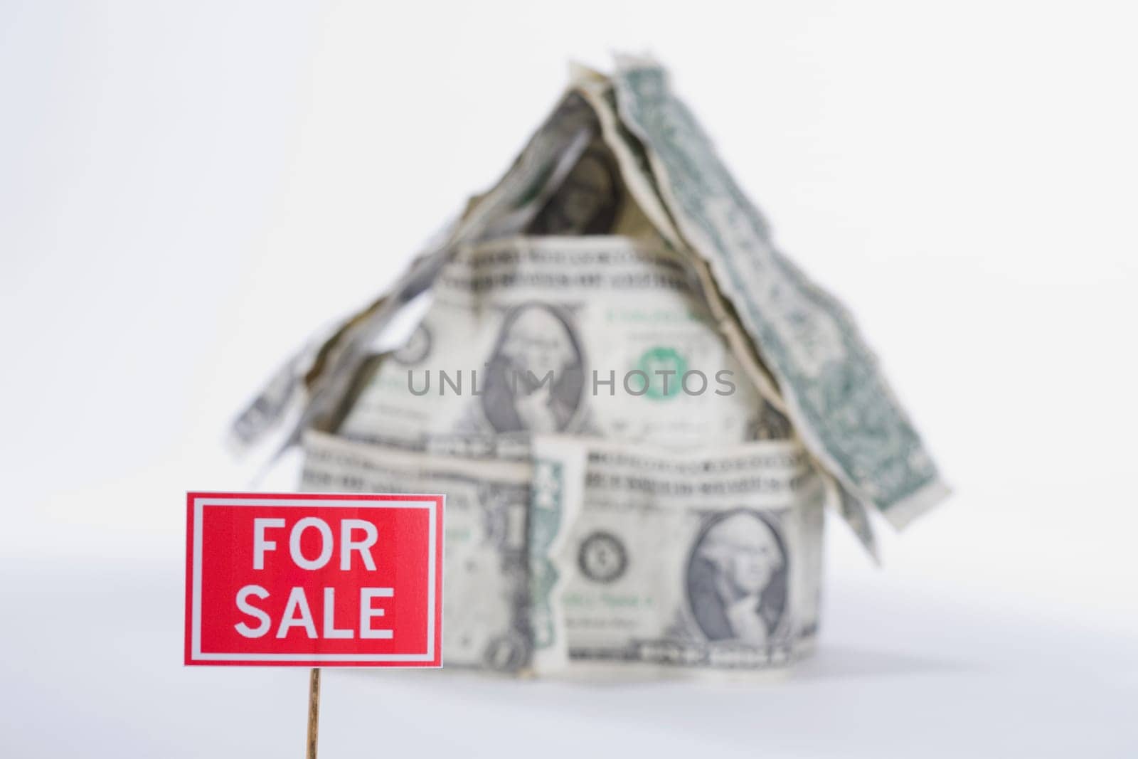 For Sale board in front of a miniature house made up of US dollar bills