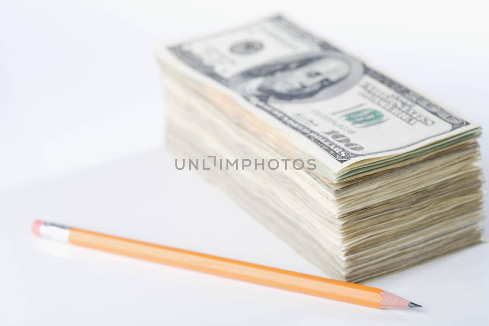 Close_up of a pencil with a bundle of paper currency