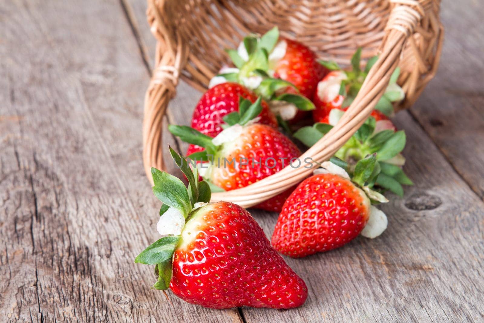 Strawberry falls from the wicker basket on a wooden background