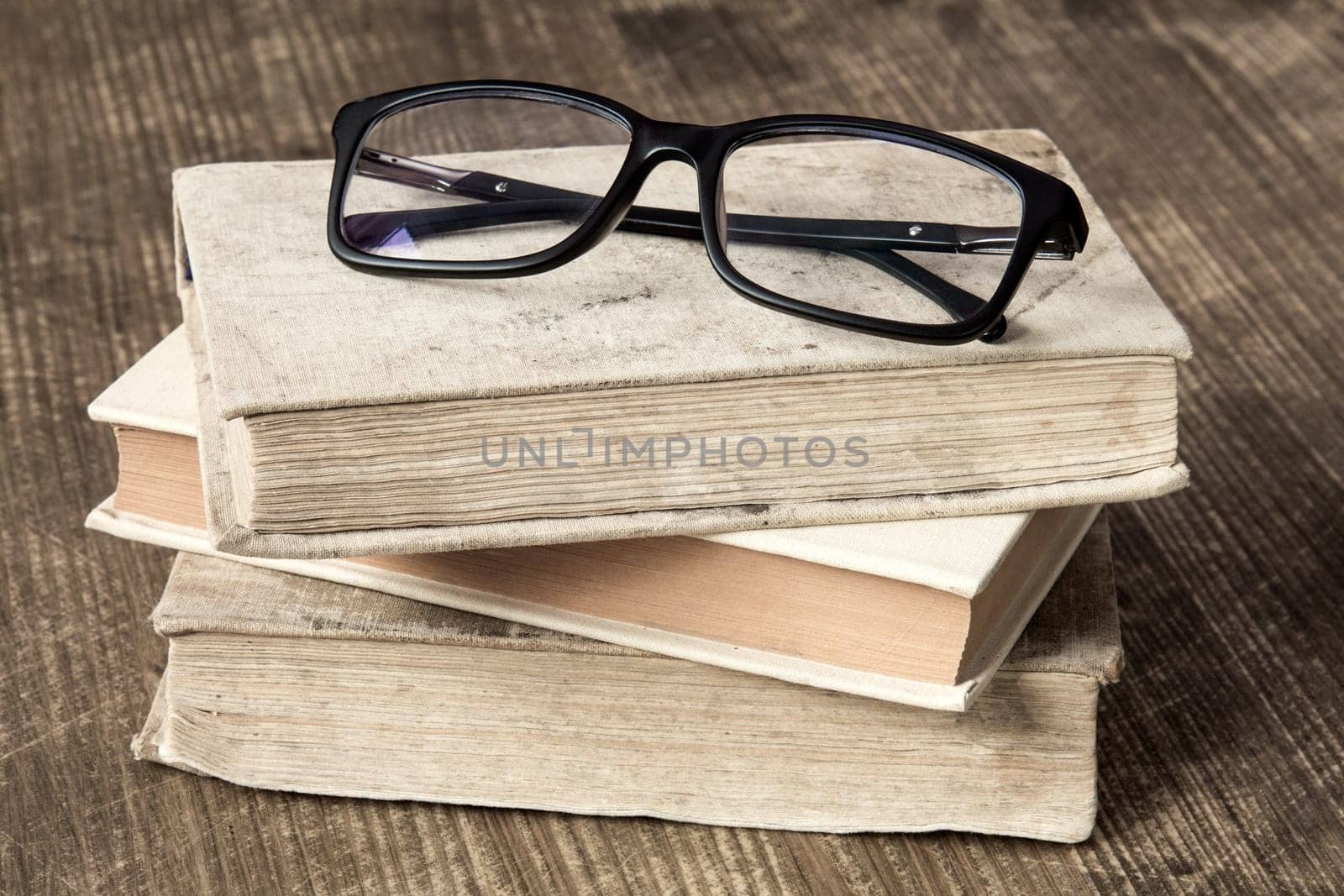Stack of books and reading glasses on the wooden background.
