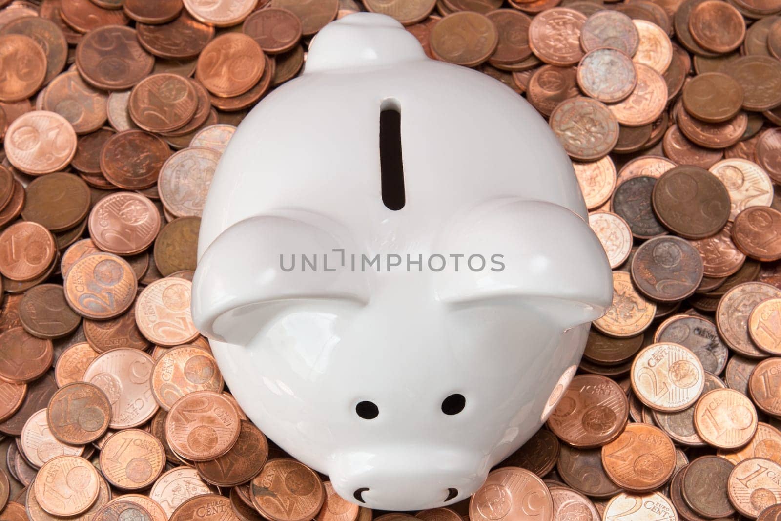 White piggy bank on pile of copper coins (Euro cents).Top view.