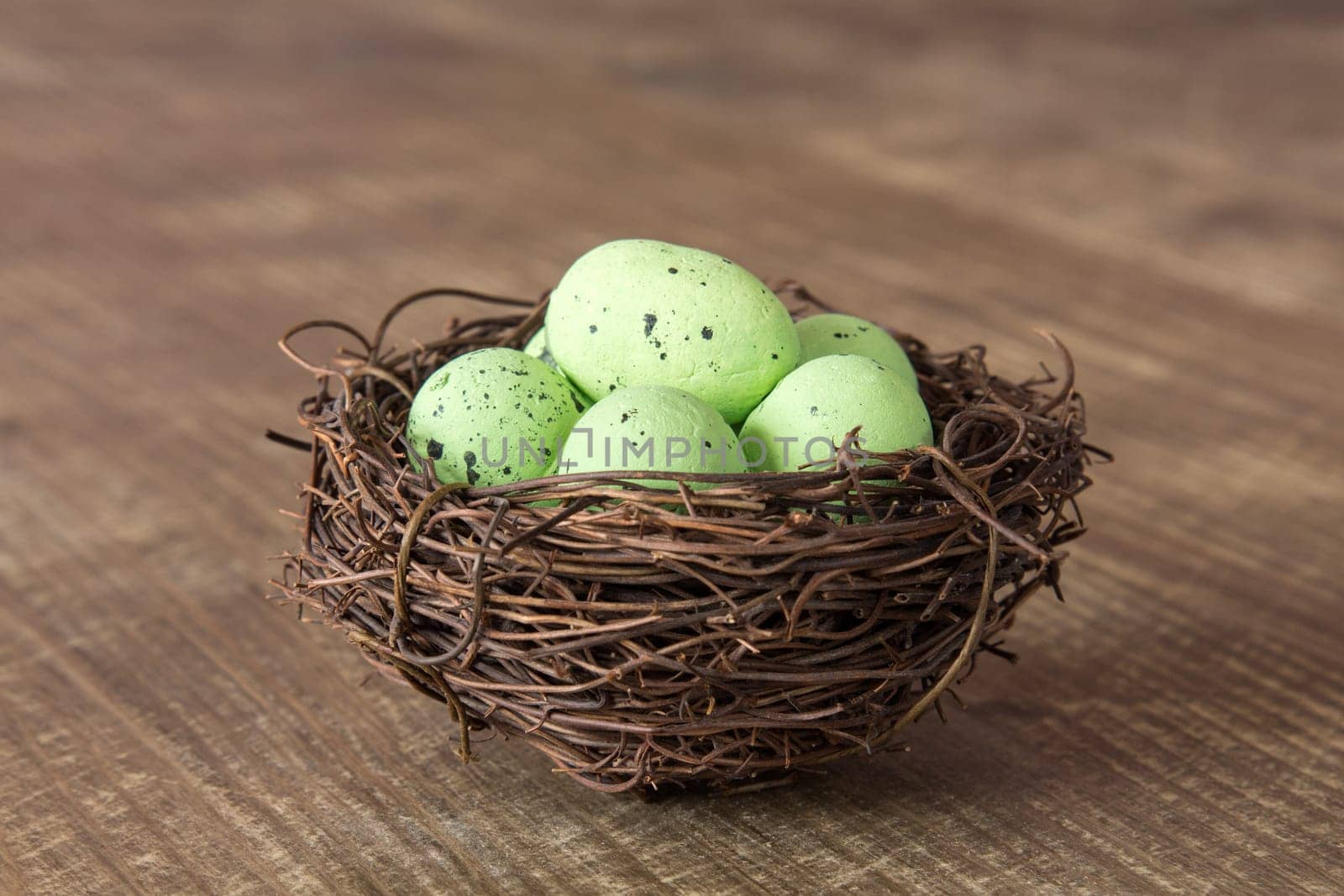 Decorative green eggs in nest on wooden background