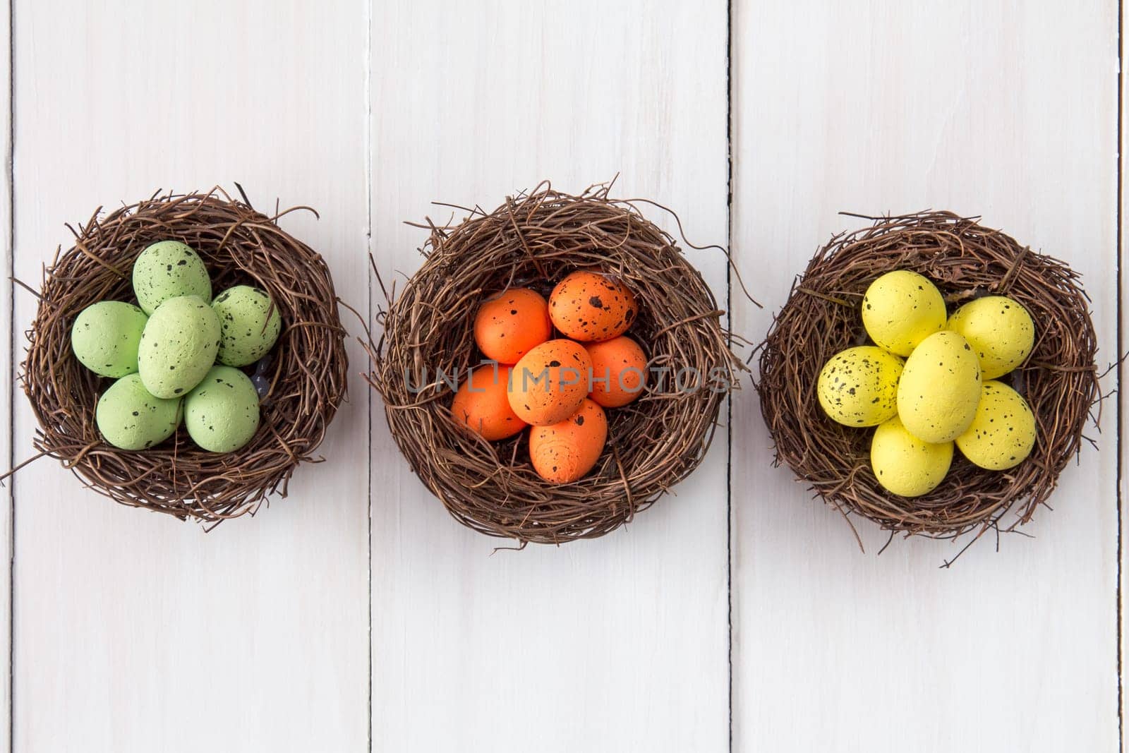 Three nests with painted  eggs on wooden background.Top view.