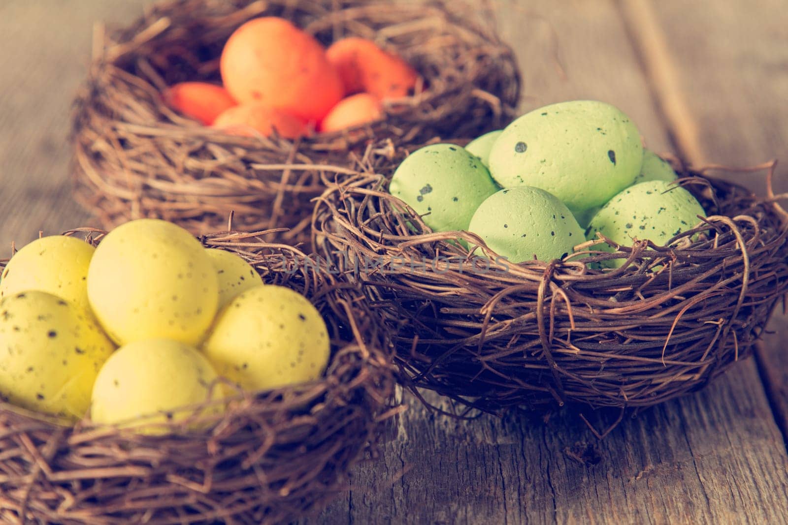 Three nests with painted eggs on wooden background. Close-up view with selective focus.