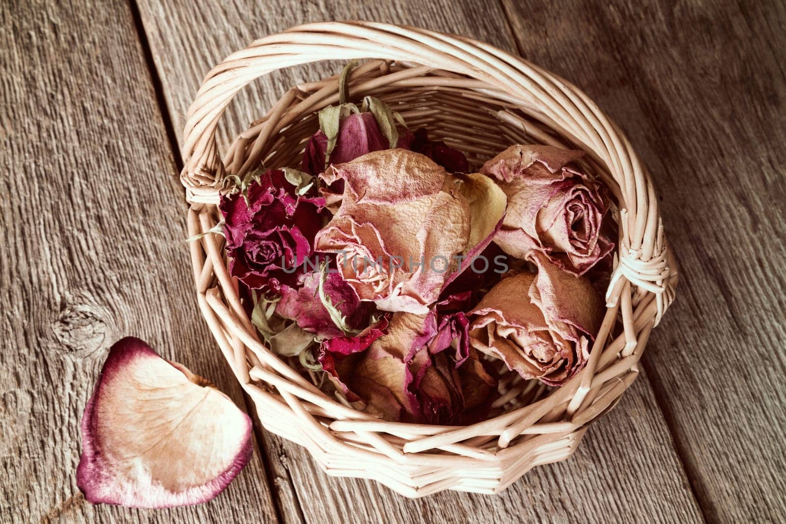 Buds of faded roses in wicker basket on wooden background