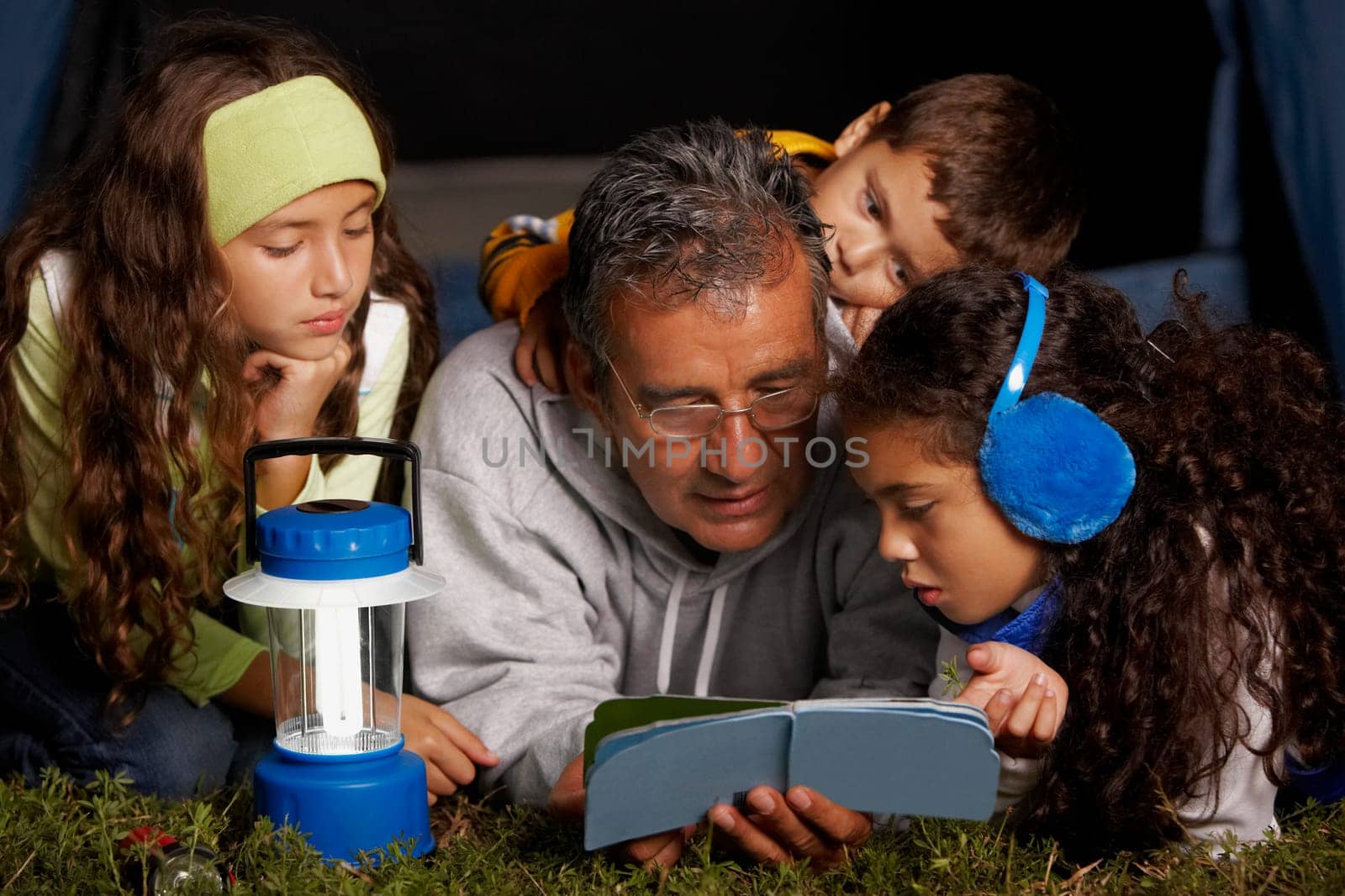 Senior man reading a book to his three grandchildren