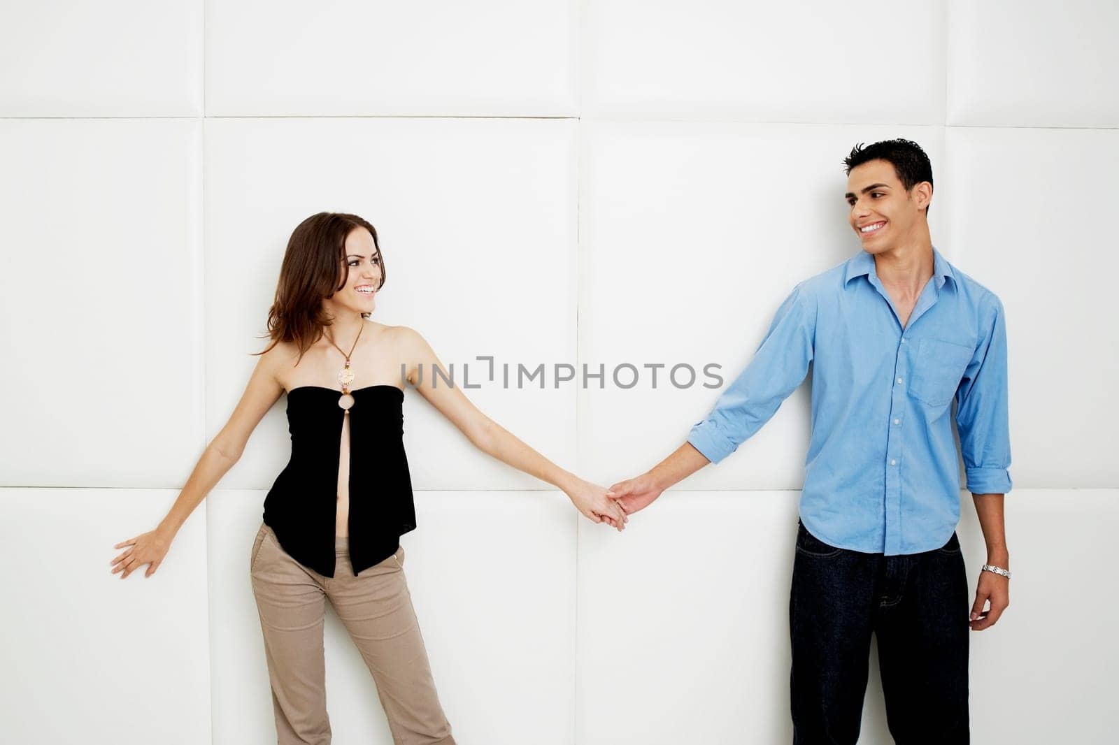 Young couple holding hands and standing beside a wall