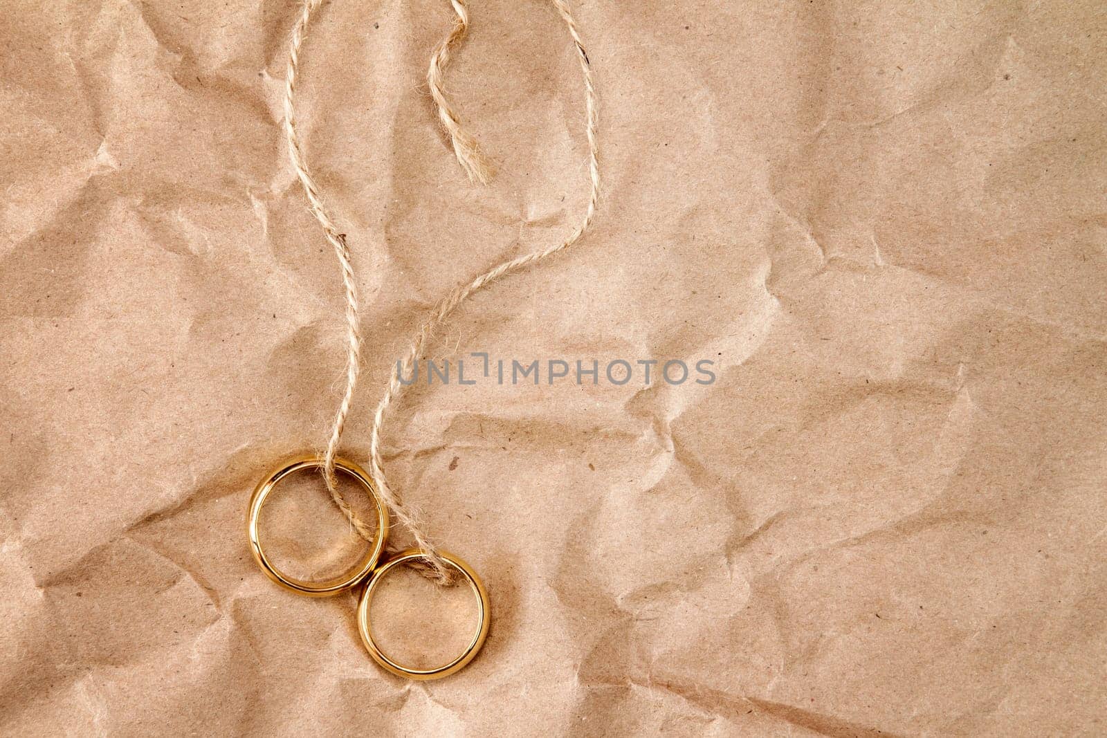 Two gold wedding rings tied with string over paper background