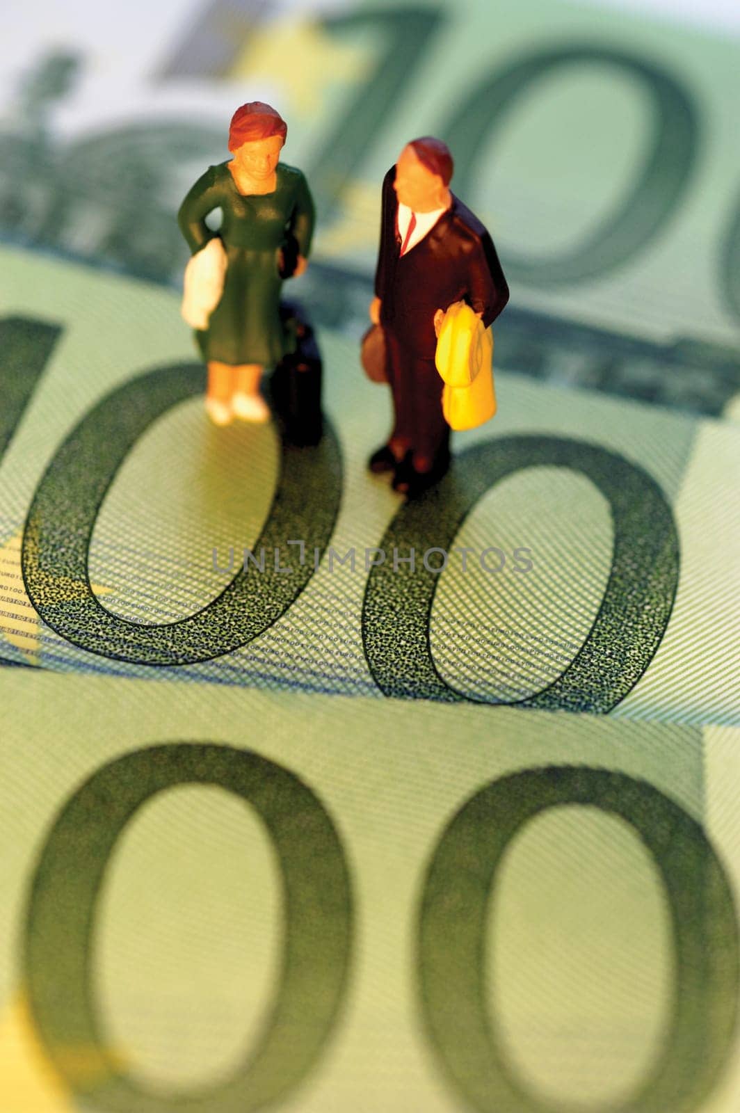 Toy businessman and businesswoman standing on top of Euro one hundred bank notes, close-up