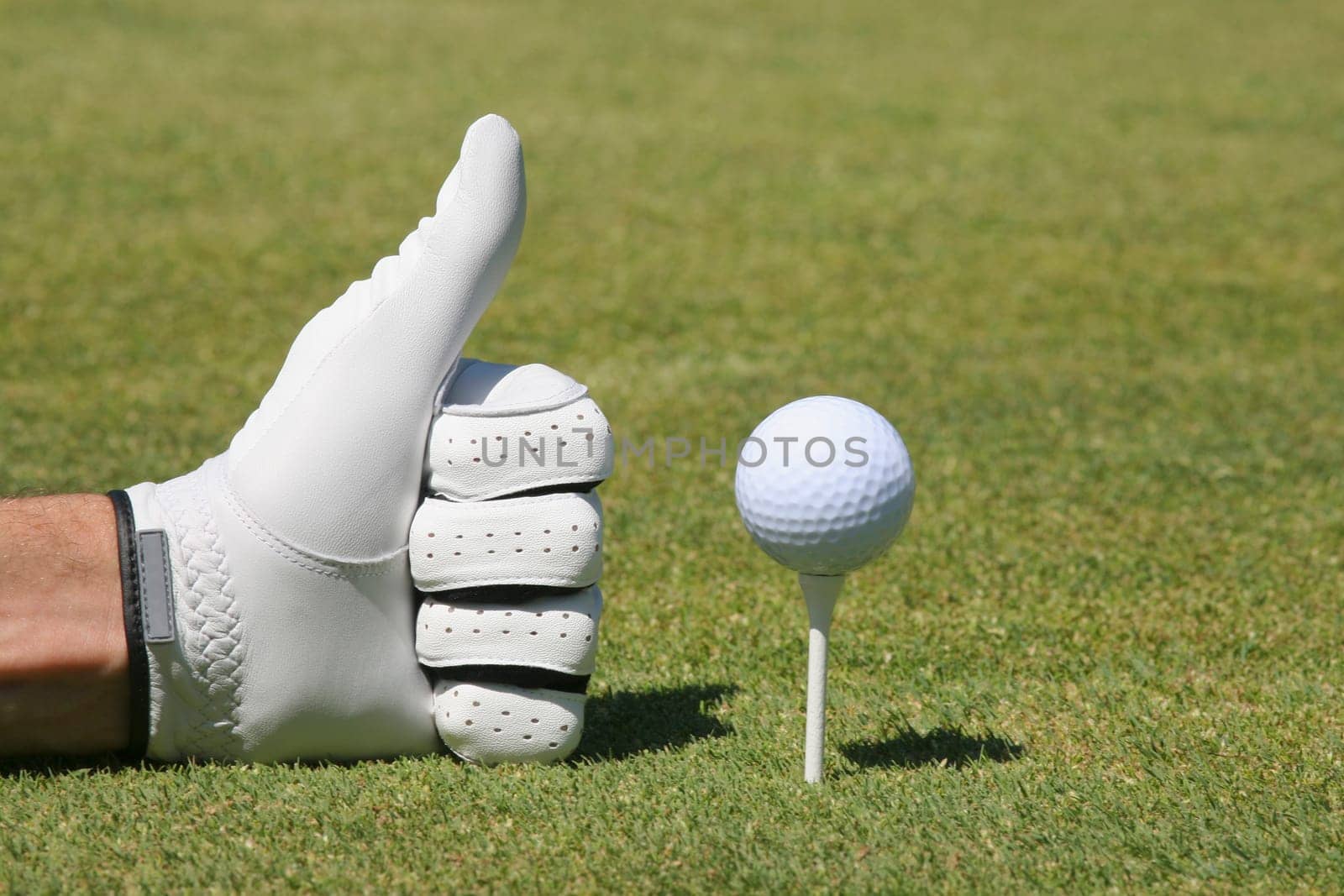 Close-up of a personŽs hand making a thumbs up sign next to a golf ball on a tee