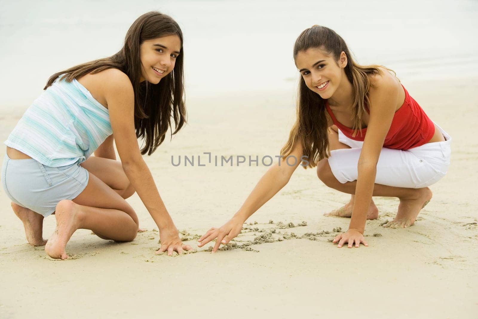 Portrait of two girls drawing in sand on the beach