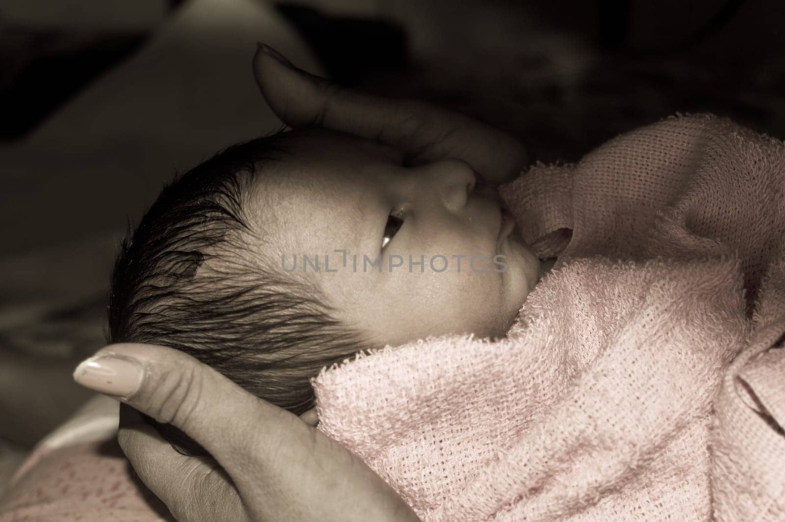 Beautiful Newborn baby boy closeup (6 days old) lying in mother lap in prenatal hospital. Kid wrapped in baby blanket (warm clothing) smiling and looking. His mother consoling and resting her baby.