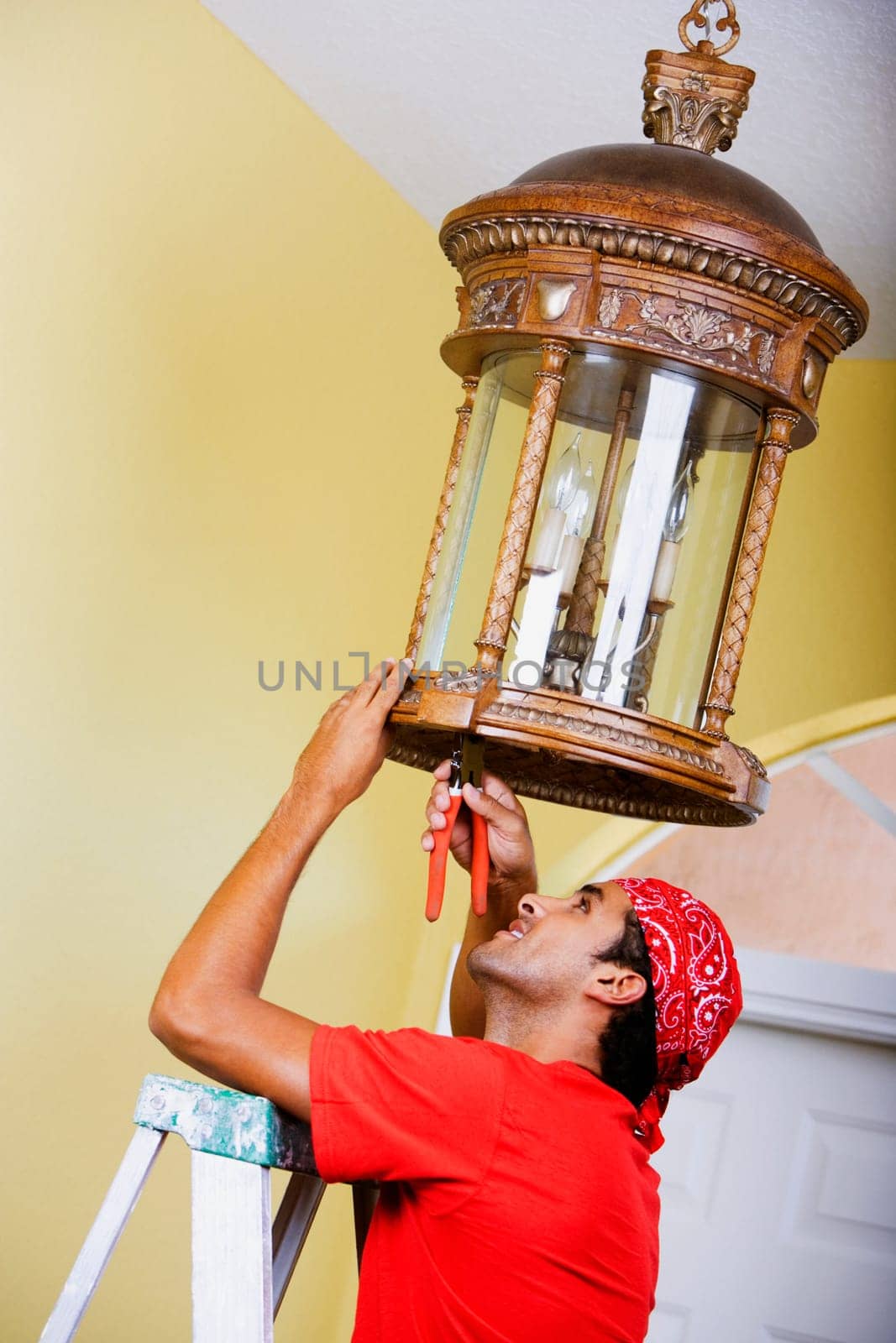 Side profile of a young man repairing a chandelier with a pair of pliers