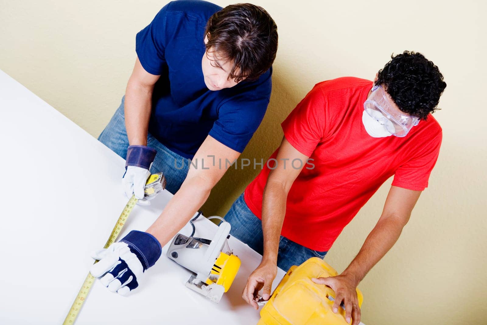 Mid adult man measuring with a measuring tape and a young man opening a toolbox