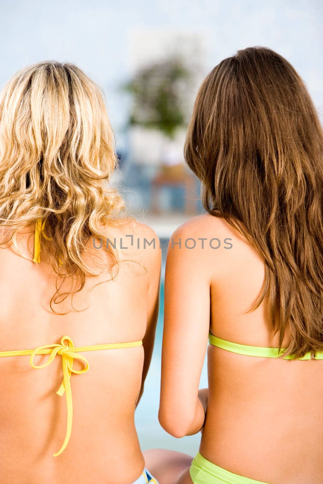 Rear view of two young women sitting at the poolside