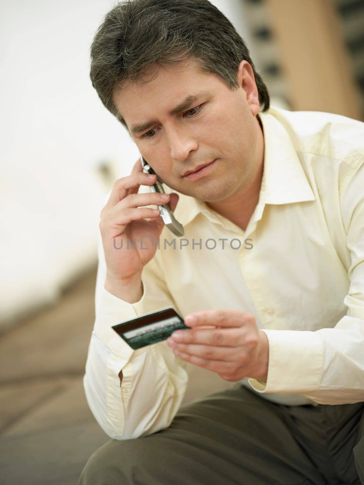 Close-up of a mature man talking on a mobile phone and holding a credit card