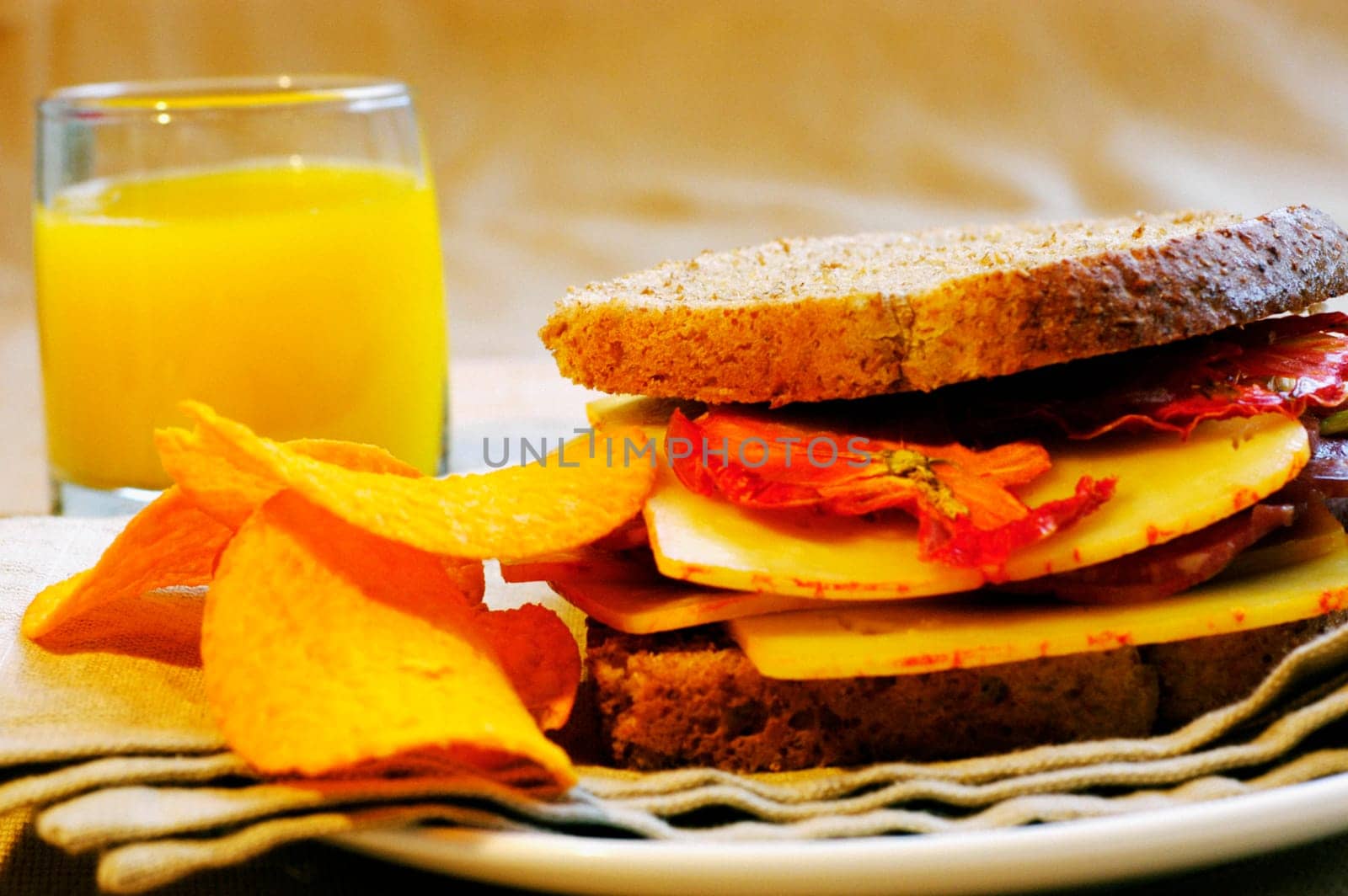 Close-up of orange juice with a sandwich and potato chips