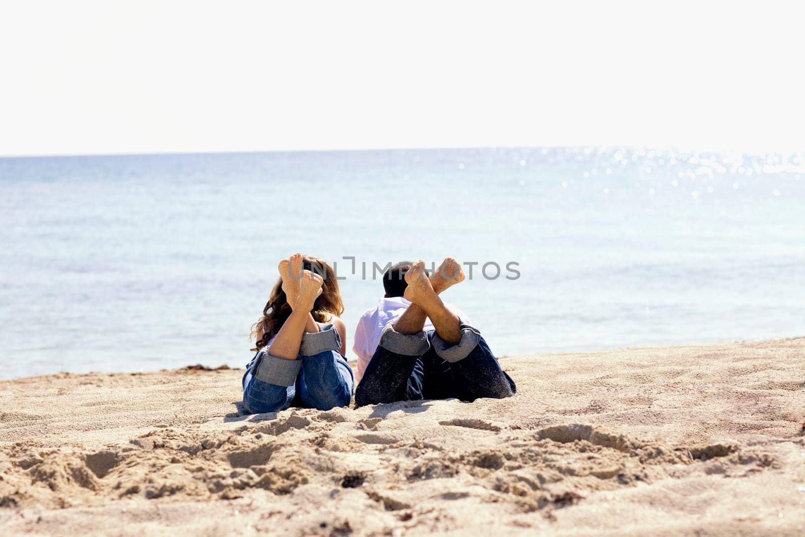 Rear view of a mid adult man and a young woman lying on the beach