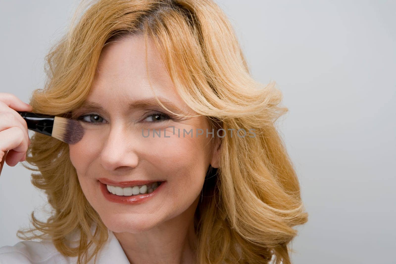 Portrait of a mature woman applying blush on her cheek and smiling