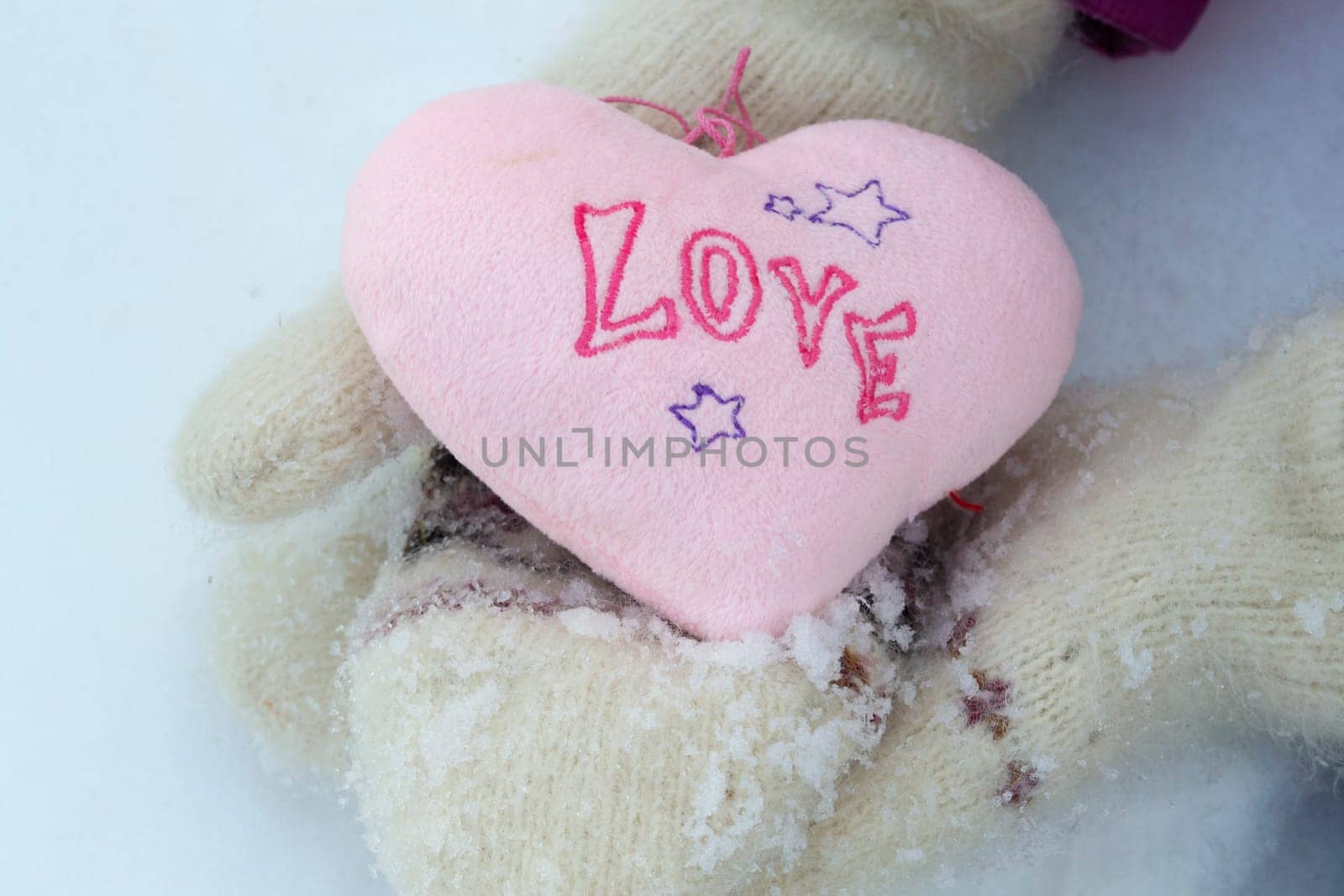 Pink heart in white warm wool gloves close up
