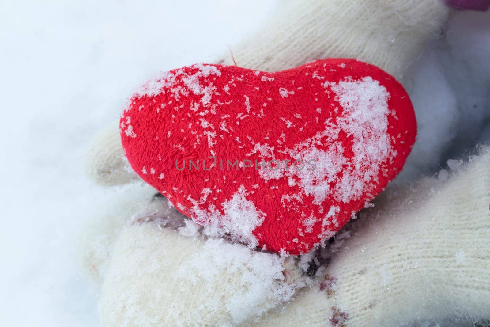 hands in white knitted mittens with a red heart on a winter day on a background of snow close up