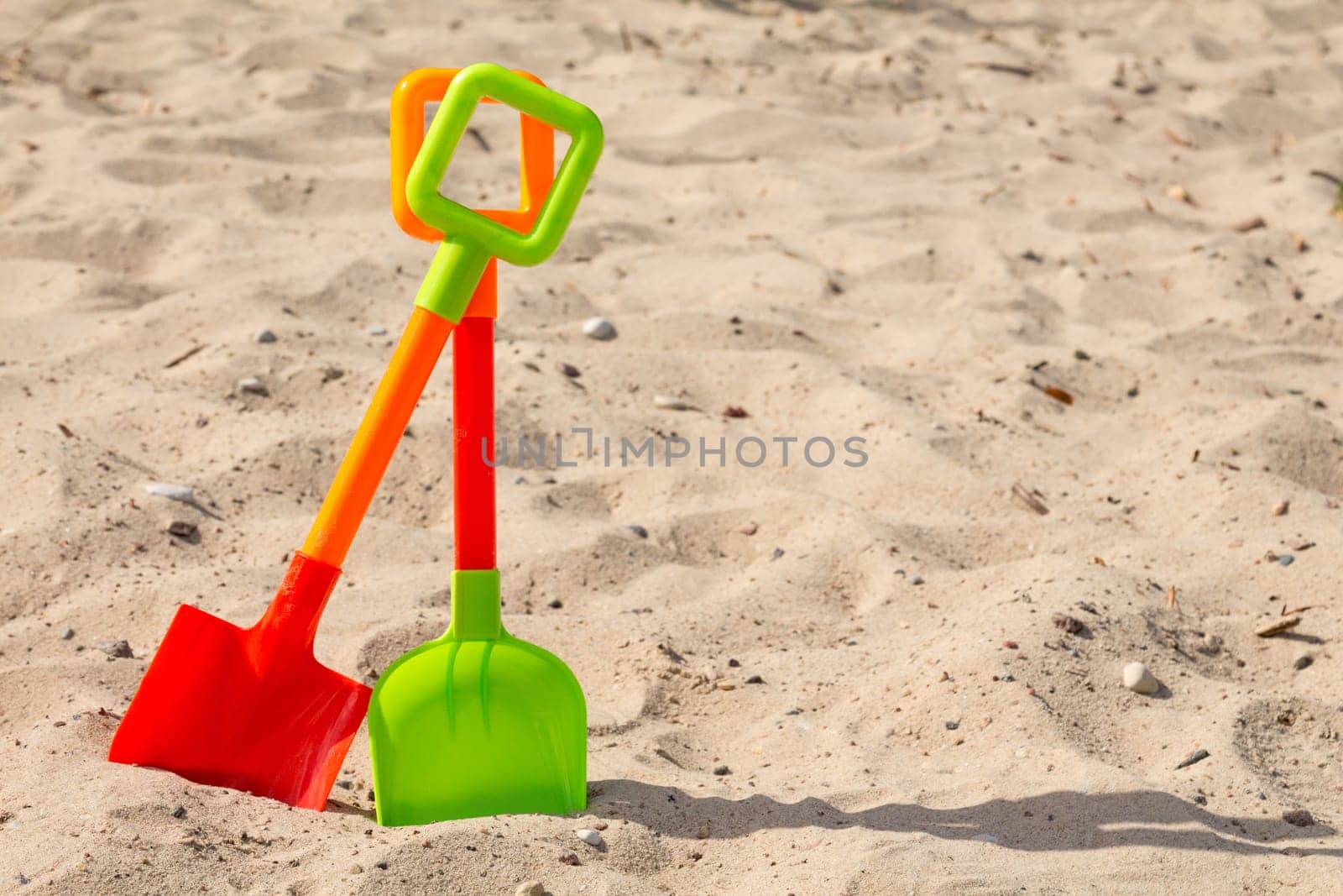 Two colorful plastic shovels on the beach sand