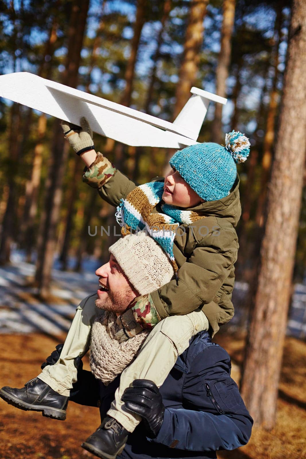 Son sitting on father's neck and holding toy plane