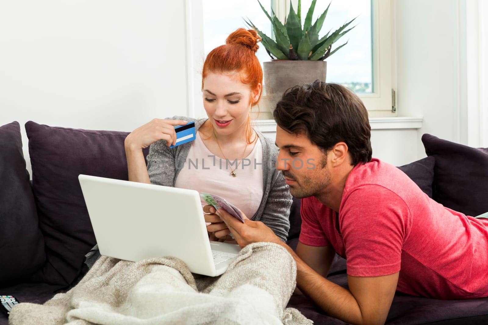 Young couple on the sofa while shopping online with cash and credit card