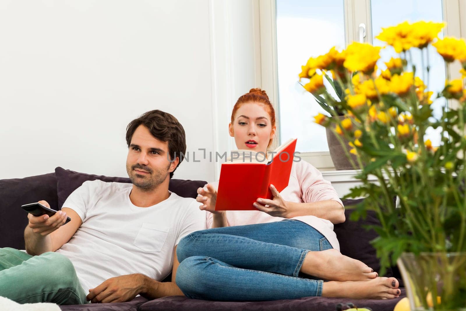 Young couple in the living room on the couch while reading and watching TV at home