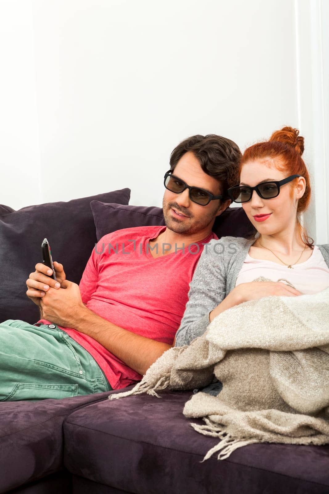 Young couple sits on the sofa with 3D glasses and looks remote concept with text freedom