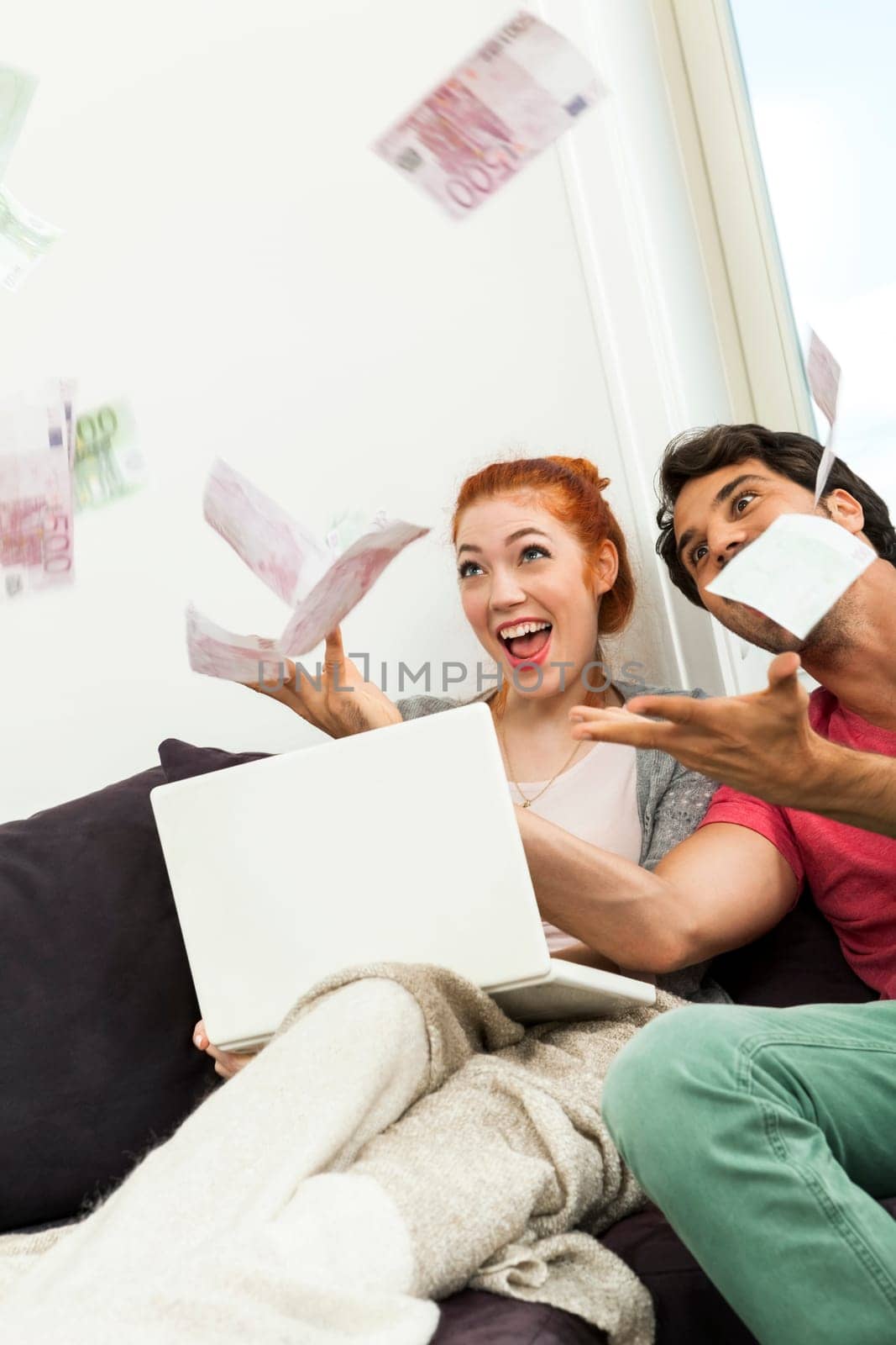 Happy boy couple with laptop on the couch throws Euro Bageld into the air concept
