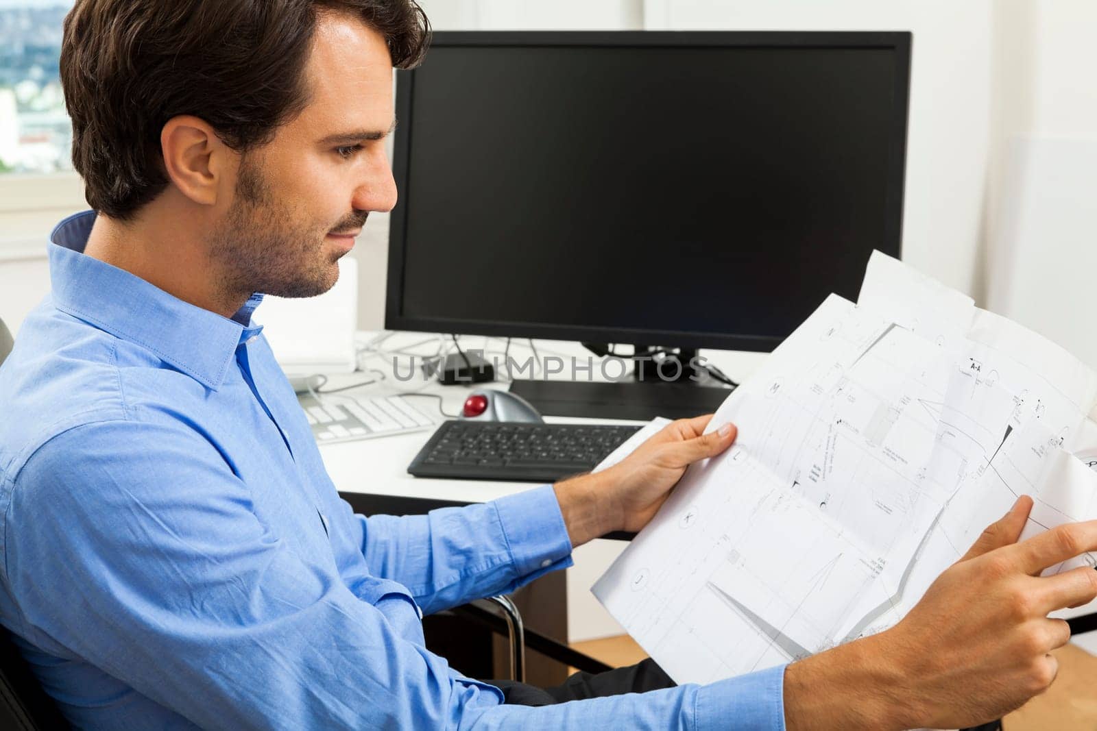 Young businessman sits with documents at a grater table in the office and informs himself