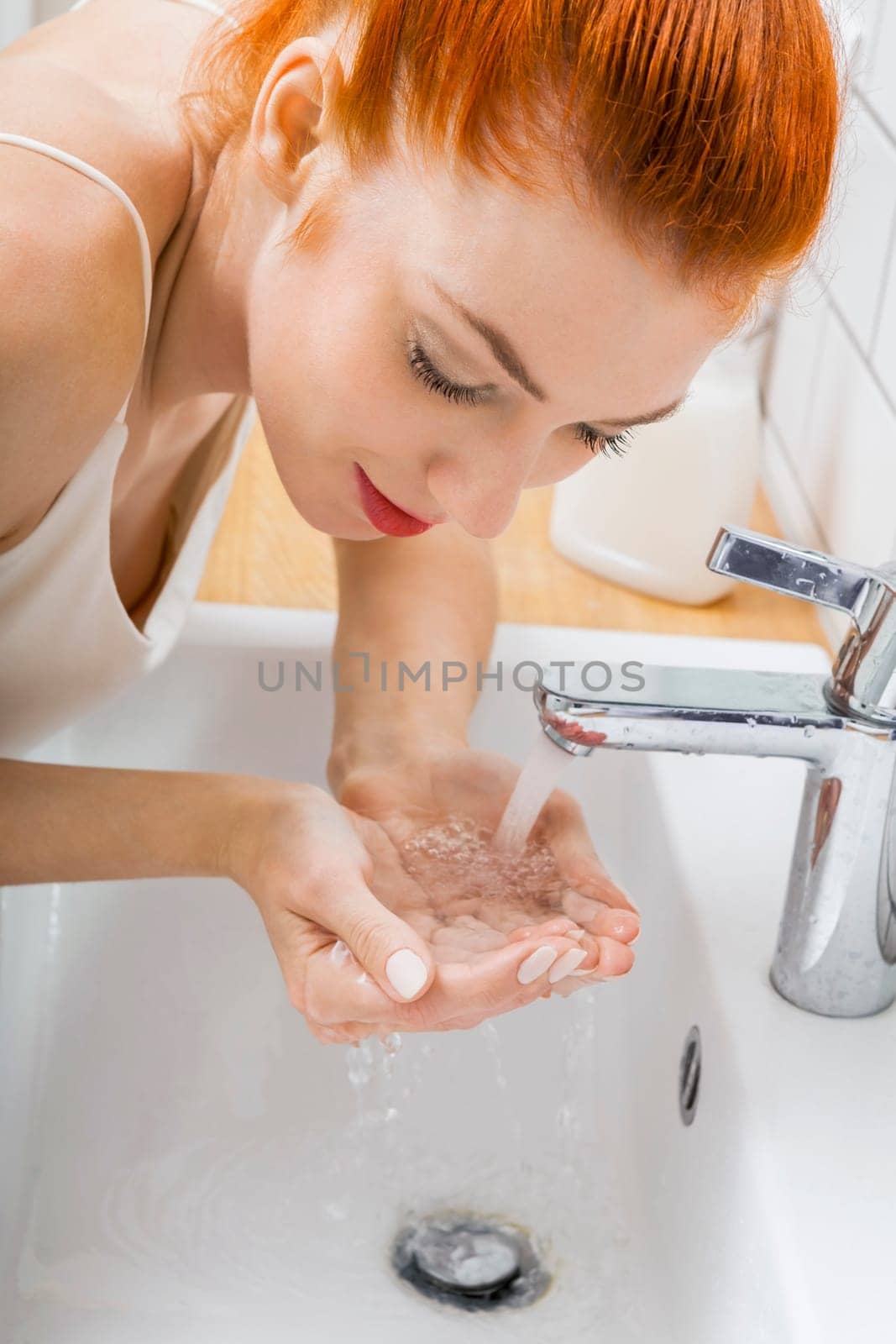 Portrait of an attractive young woman with red hair in the morning in the bathroom while washing face skin care