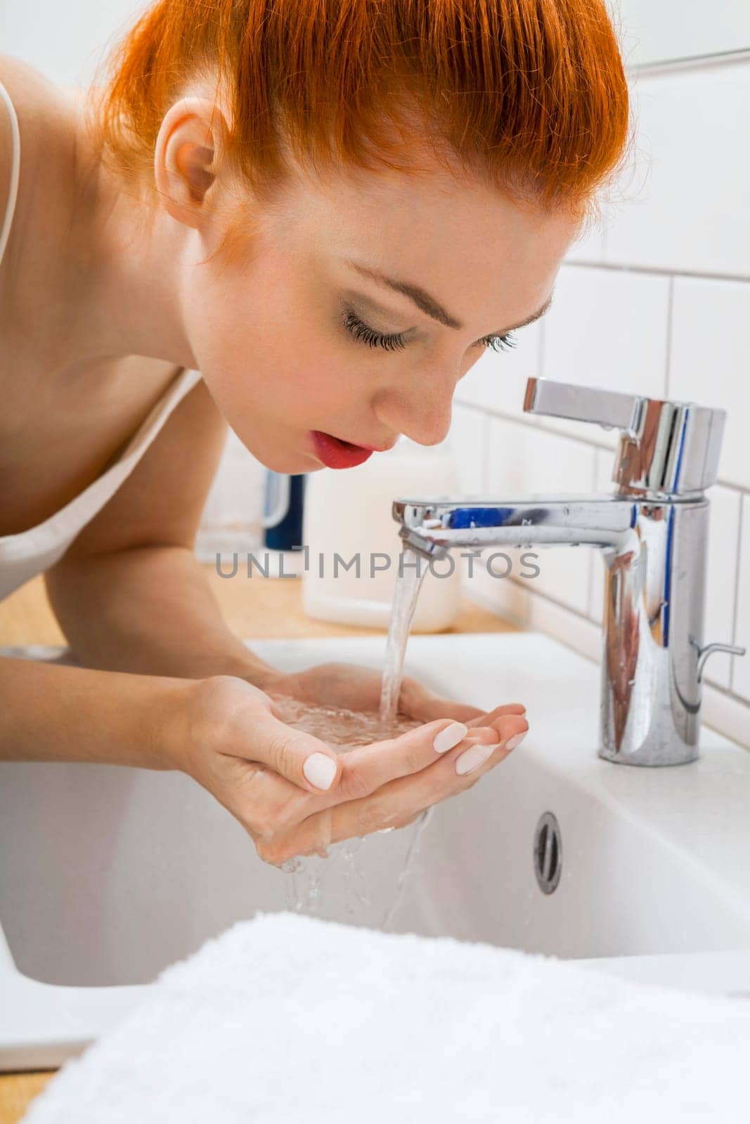 Portrait of an attractive young woman with red hair in the morning in the bathroom while washing face skin care
