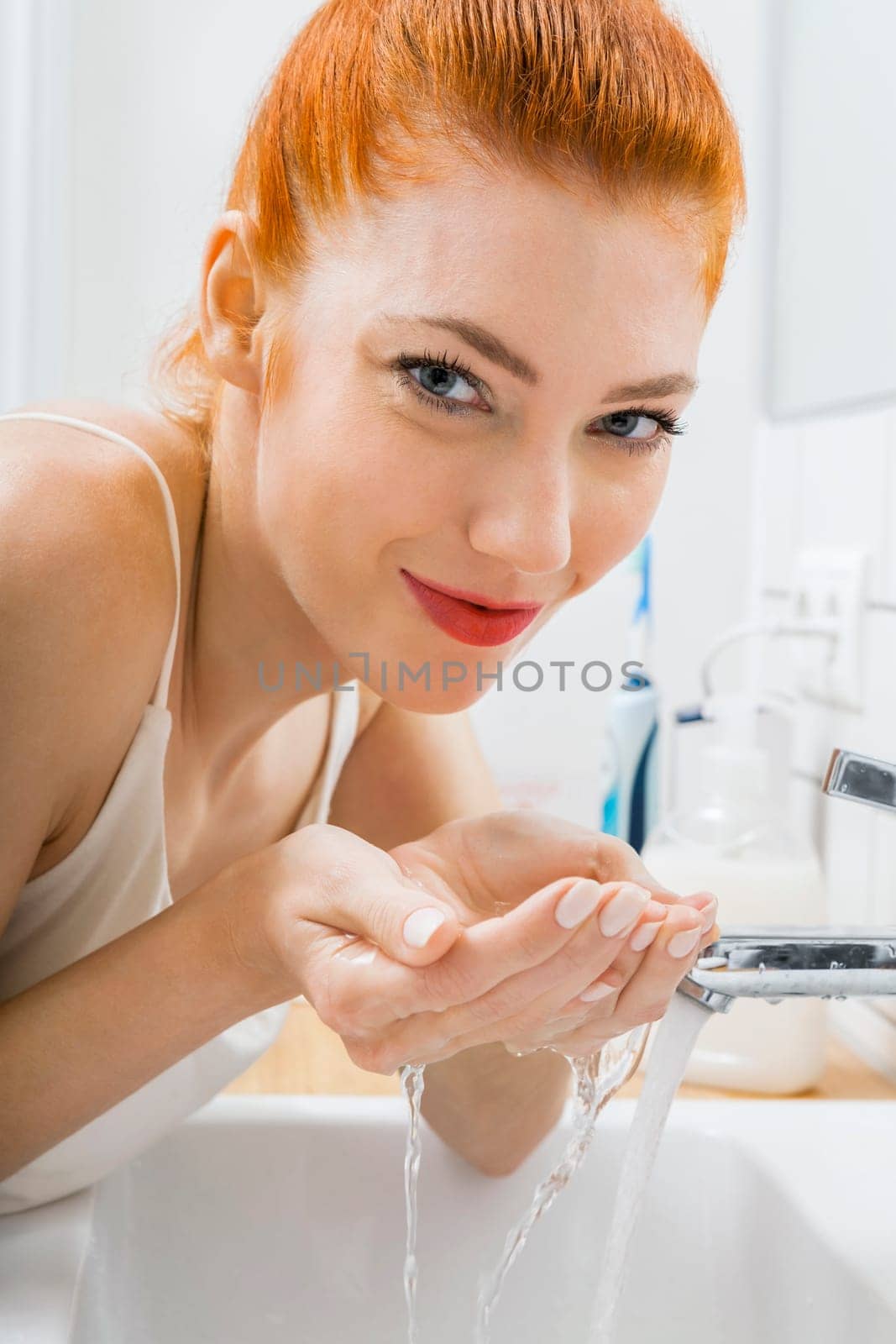 Portrait of an attractive young woman with red hair in the morning in the bathroom while washing face skin care